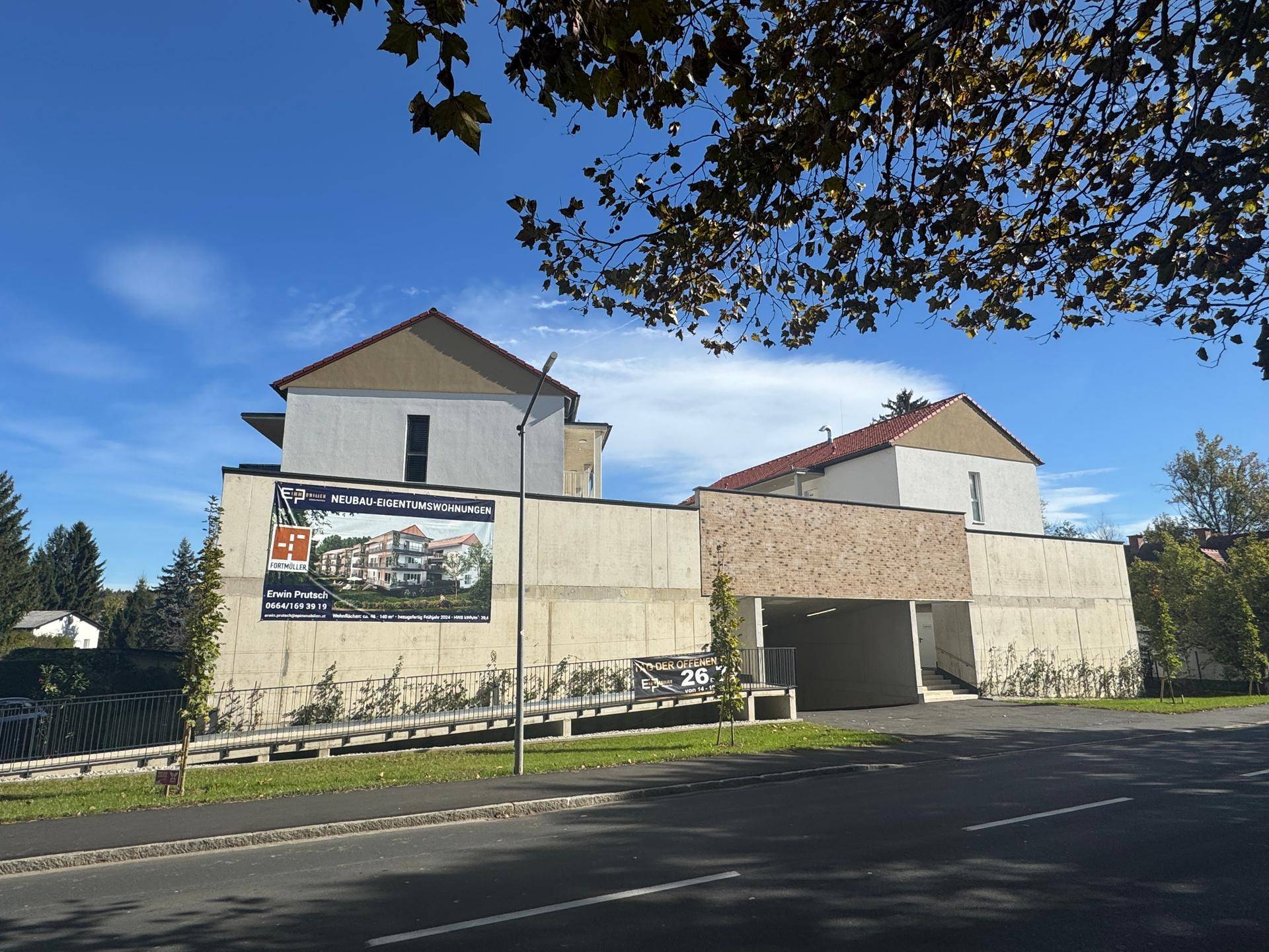 Moderne Gebäudefassade mit Werbebanner für Neubau-Eigentumswohnungen und Tiefgaragenzufahrt.