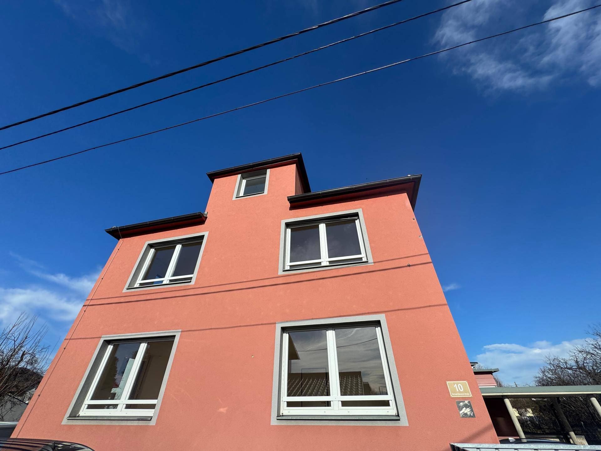 Rotes Mehrfamilienhaus mit mehreren Fenstern unter blauem Himmel.