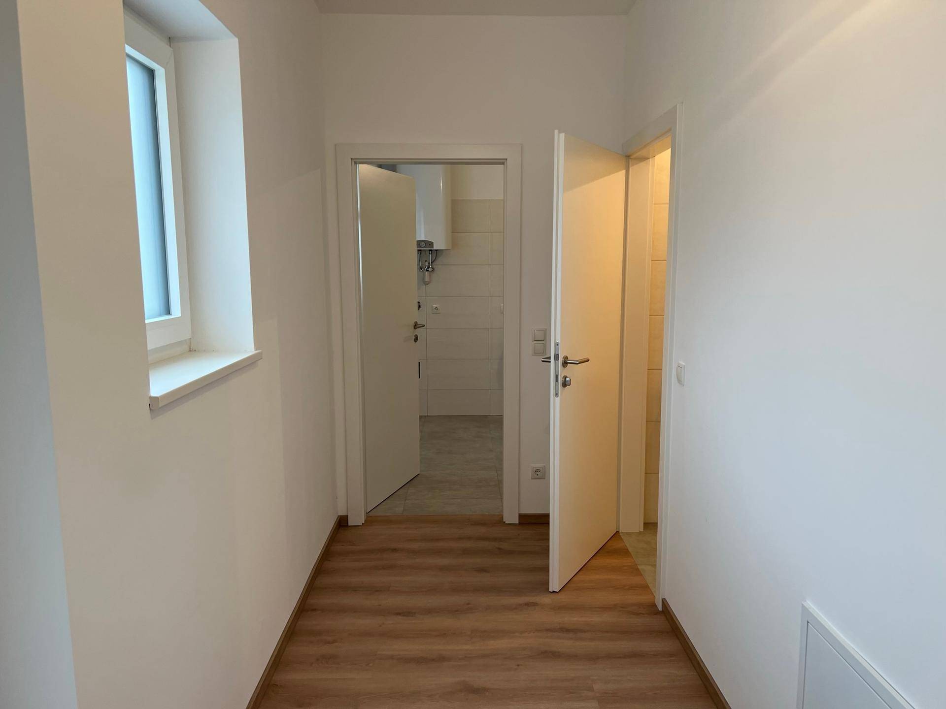 Heller Flur mit Laminatboden und mehreren weißen Türen, die zu verschiedenen Zimmern führen.