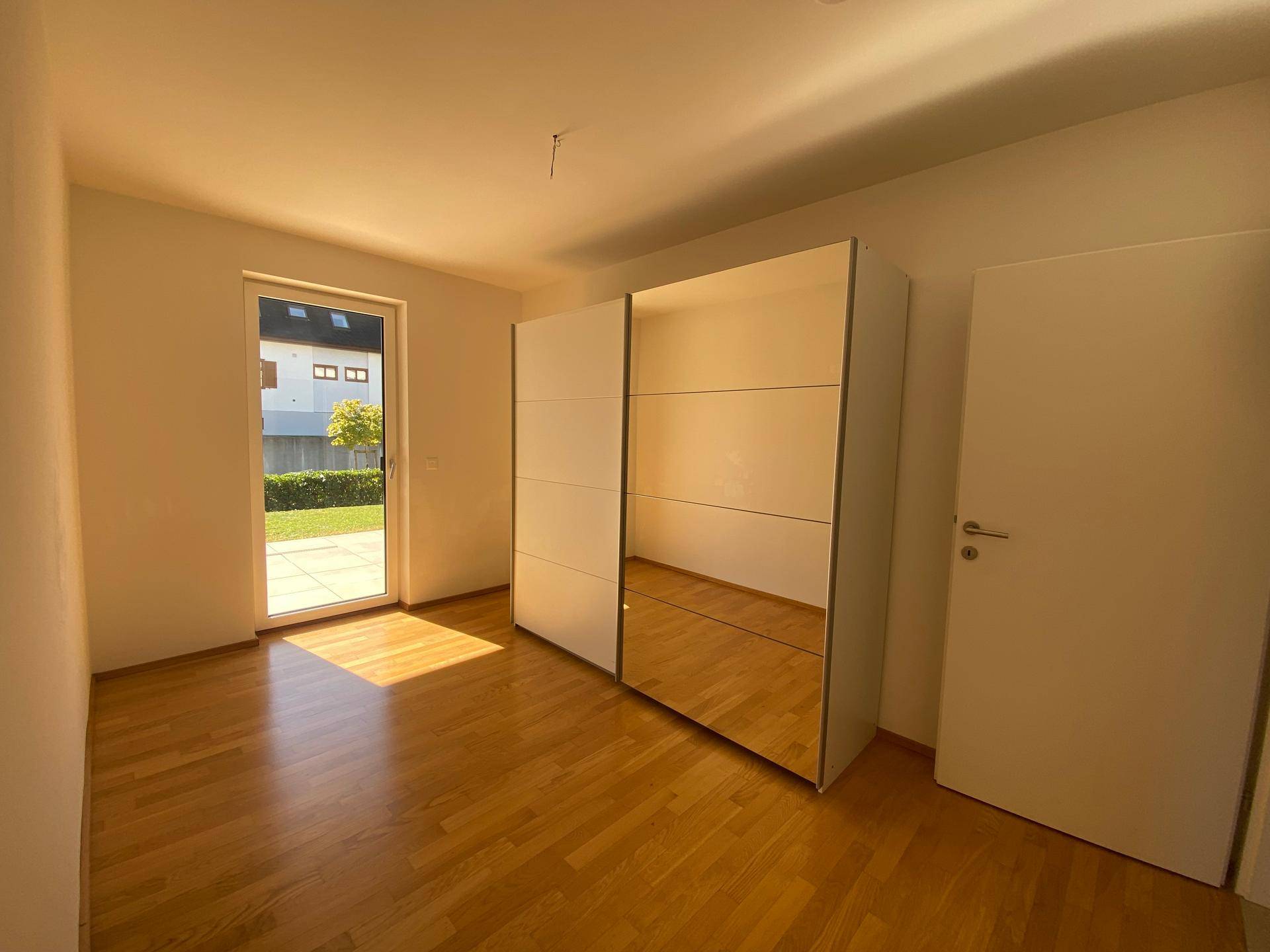Schlafzimmer mit Holzboden, Spiegelschrank und Zugang zu einer kleinen Terrasse oder Garten.