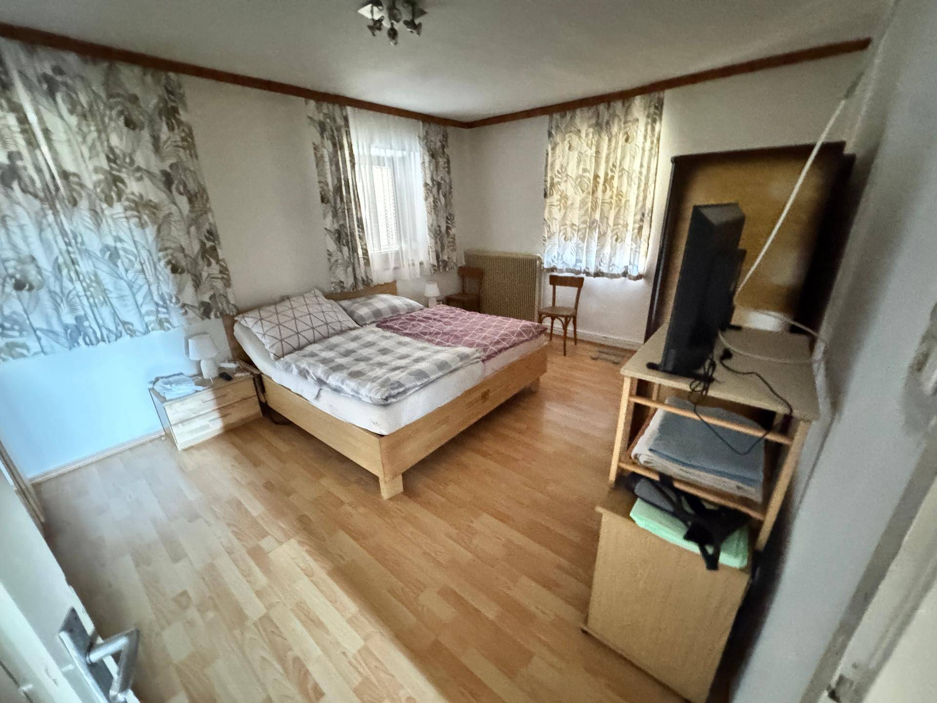 Schlafzimmer mit Holzbett, Parkettboden und gemusterten Vorhängen, bietet eine gemütliche Atmosphäre.