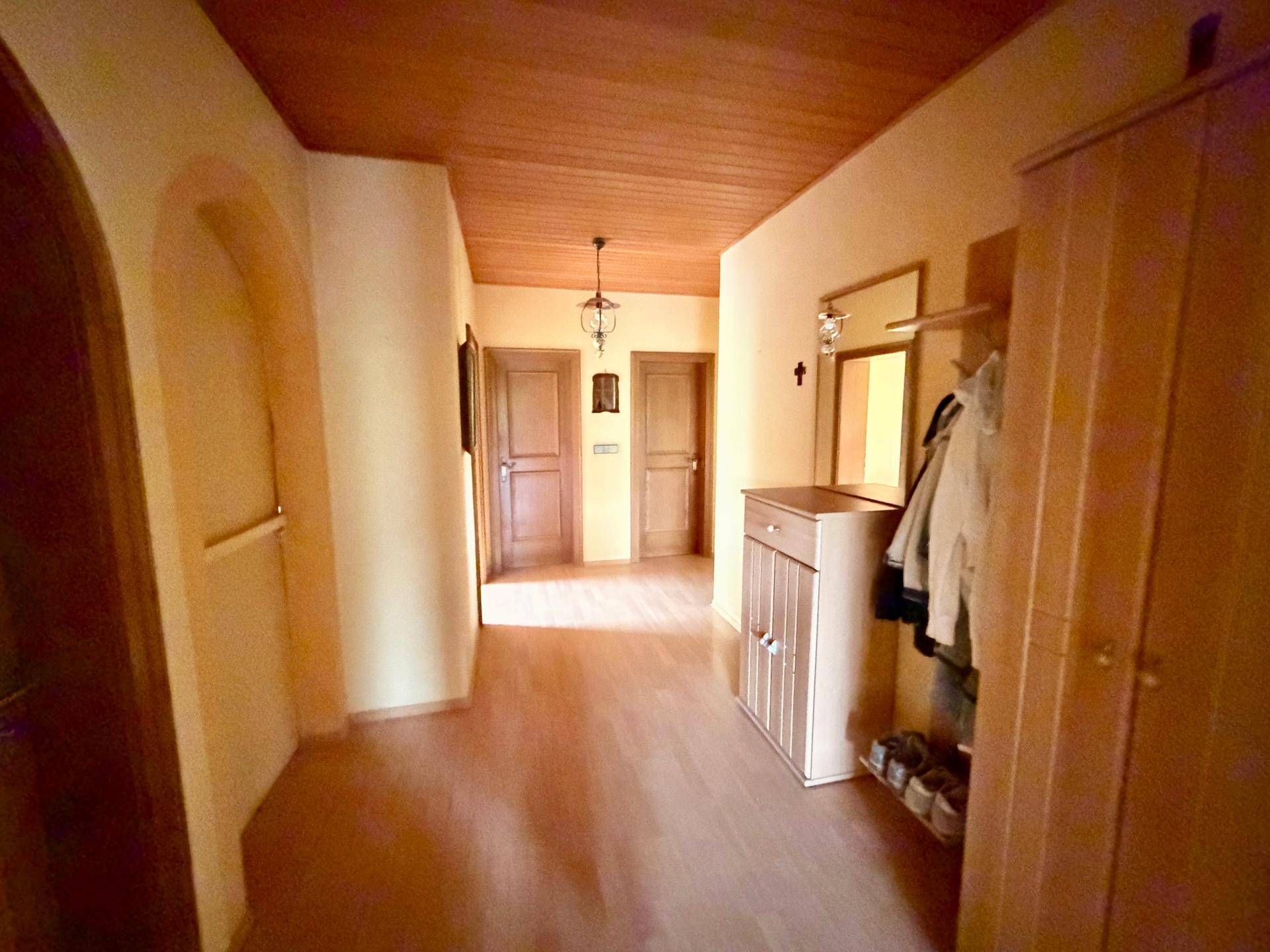 Heller Flur mit Holzdecke, Laminatboden und Garderobe, der zu weiteren Räumen führt.