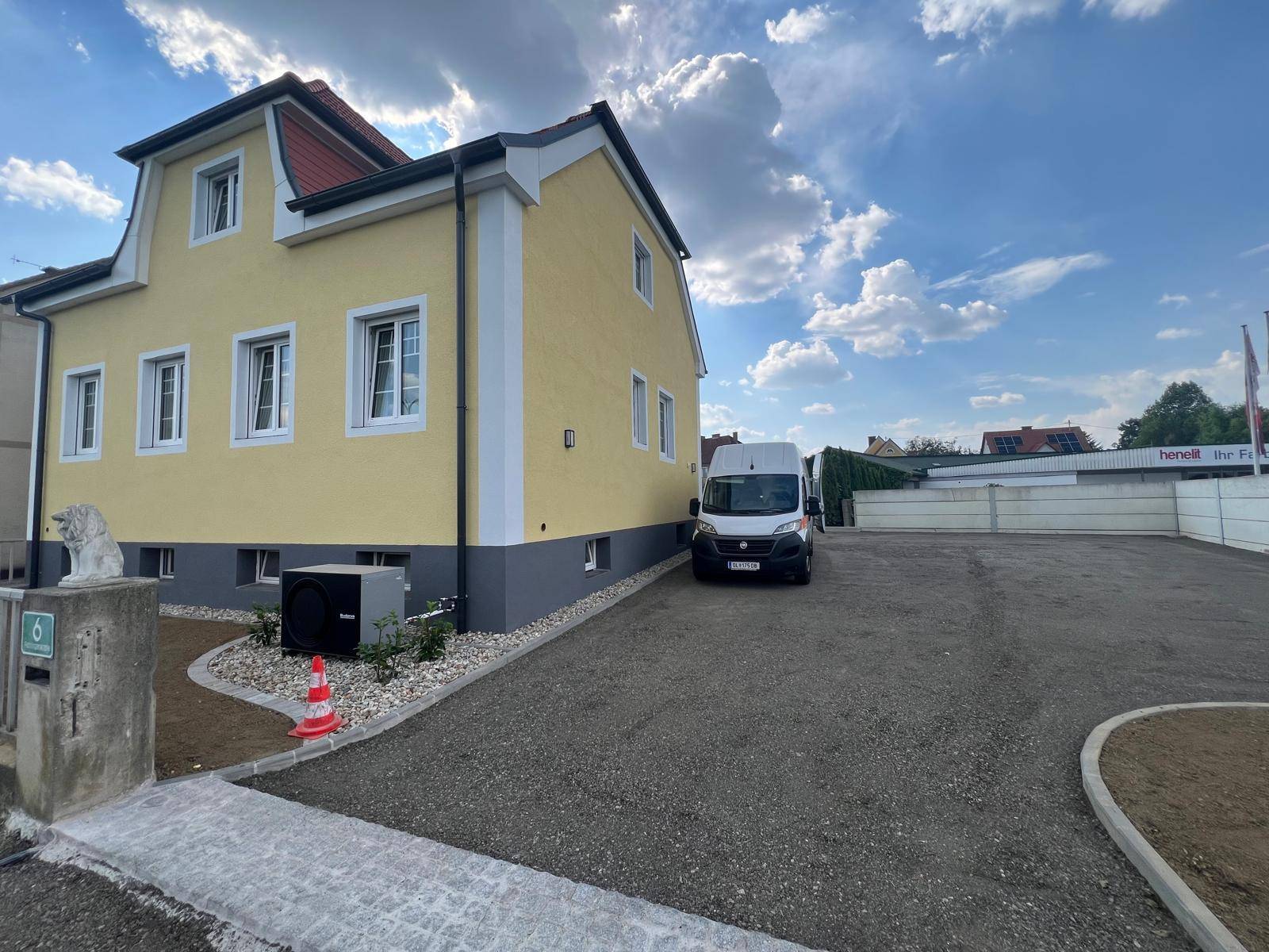 Frisch renoviertes Haus mit gelber Fassade und großem Schotterparkplatz.