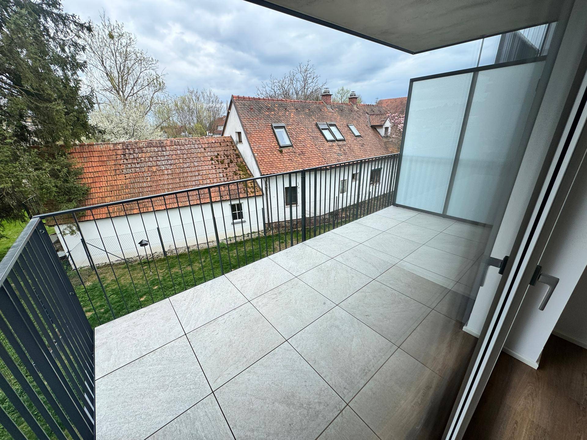 Balkon mit Fliesenboden und Blick auf grüne Umgebung und traditionelle Häuser.