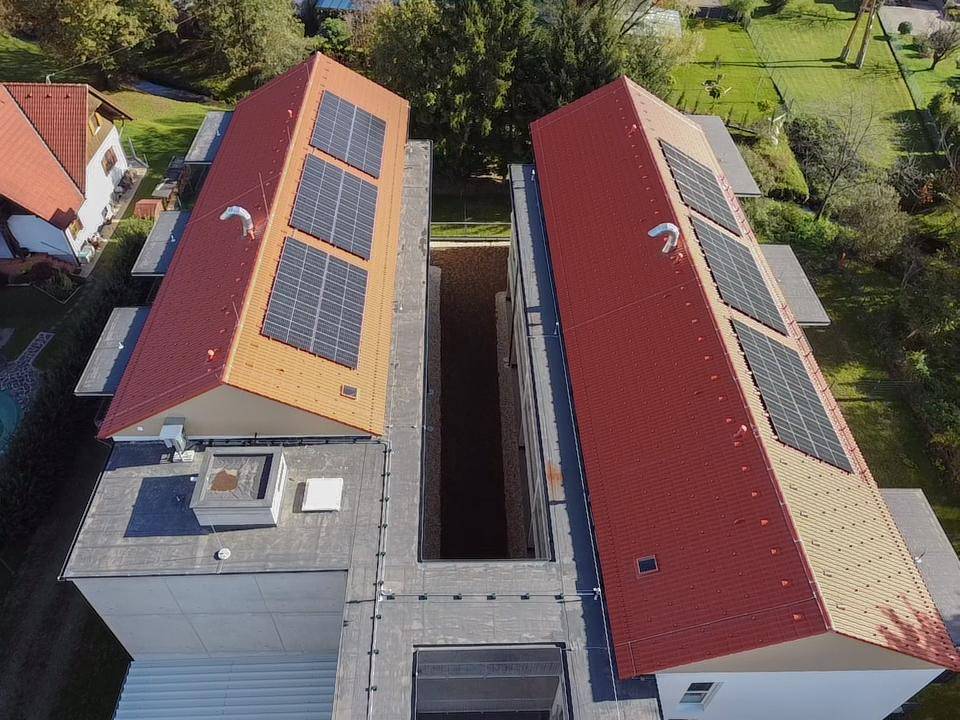 Luftaufnahme von zwei Gebäuden mit roten Dächern und Photovoltaikanlagen.