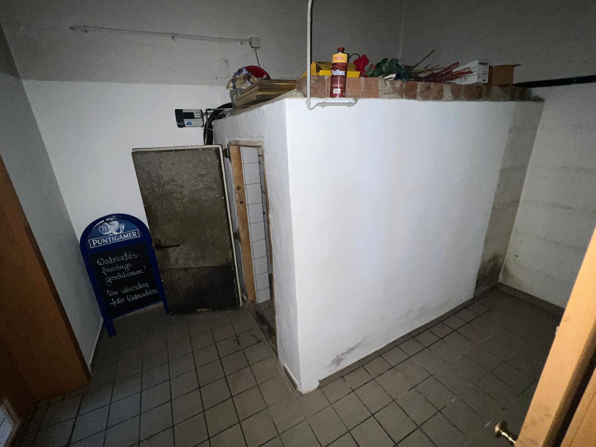 Kleiner Lagerraum mit gefliestem Boden und einer weißen, gemauerten Struktur in der Mitte.