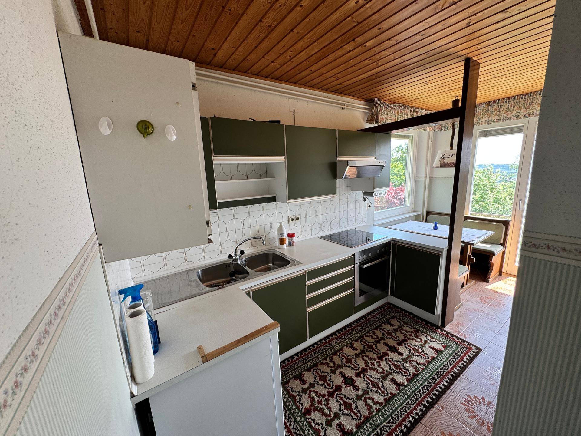Kleine Küche mit olivgrünen Schränken, Holzdecke und Blick ins Grüne.