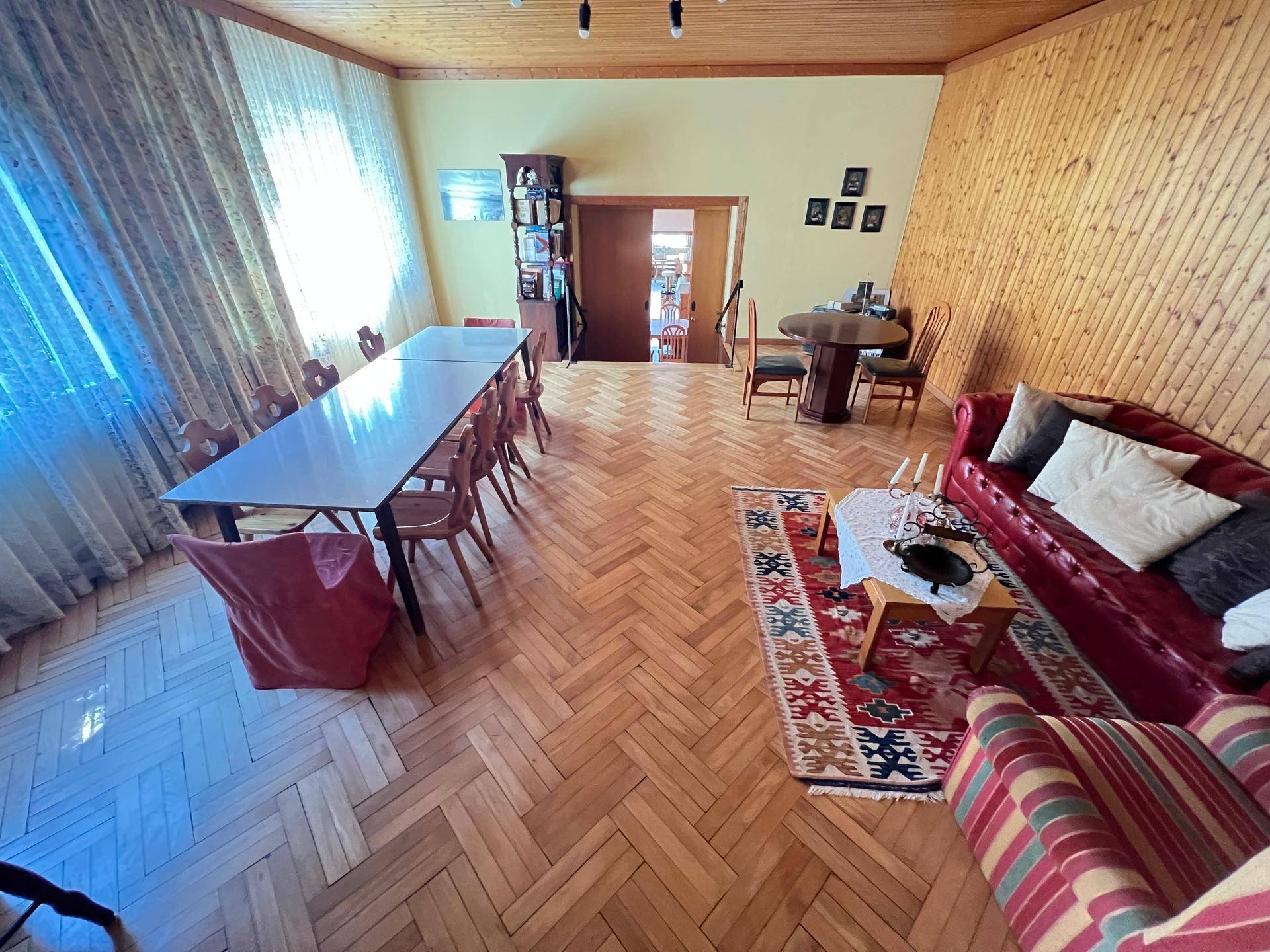 Geräumiger Wohn- und Essbereich mit Holzboden, Holzvertäfelung und rotem Sofa.