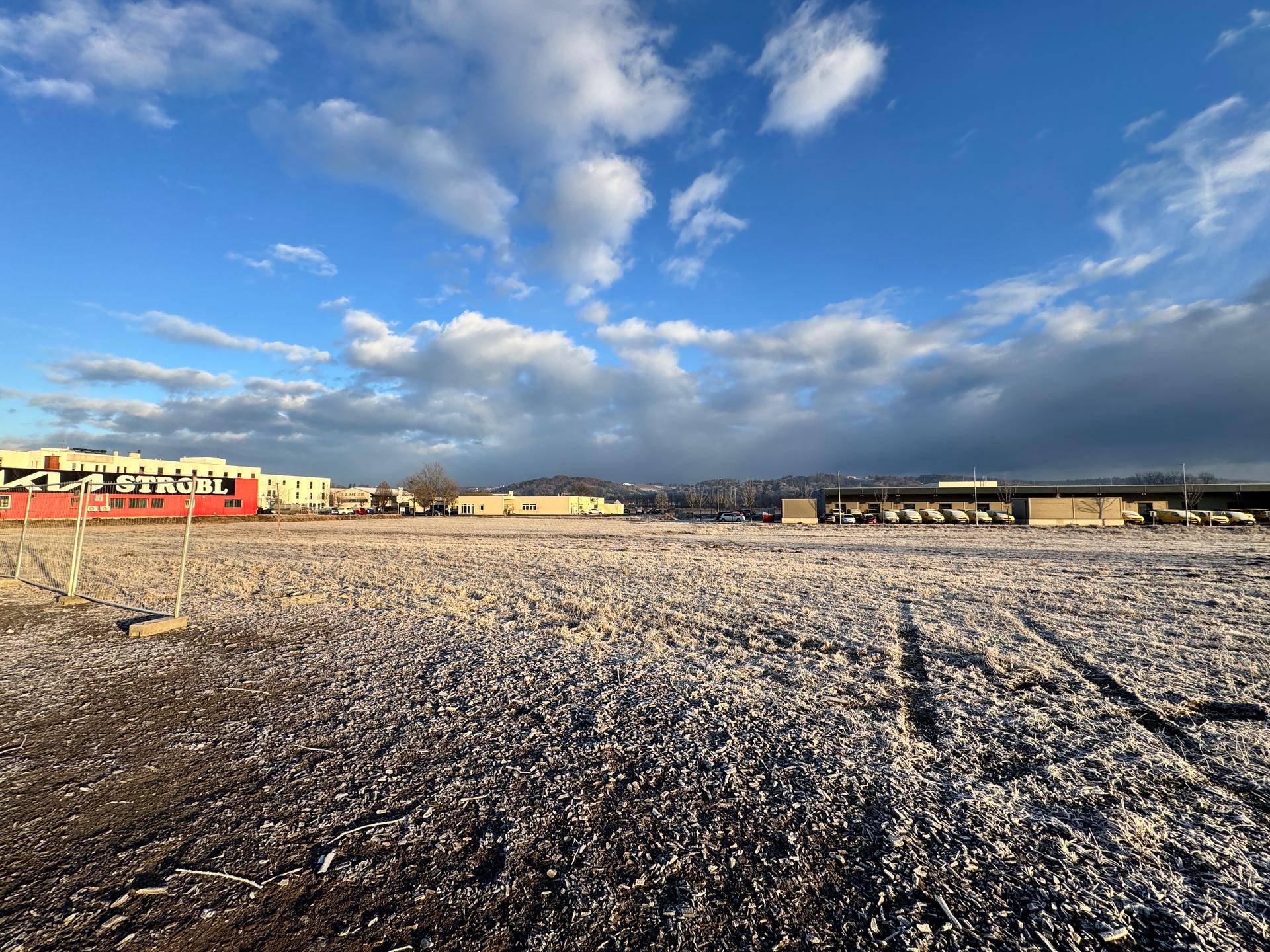Weitläufiges, frostbedecktes Feld mit Gewerbegebäuden und dem 'STROBL'-Gebäude im Vordergrund unter blauem Himmel.