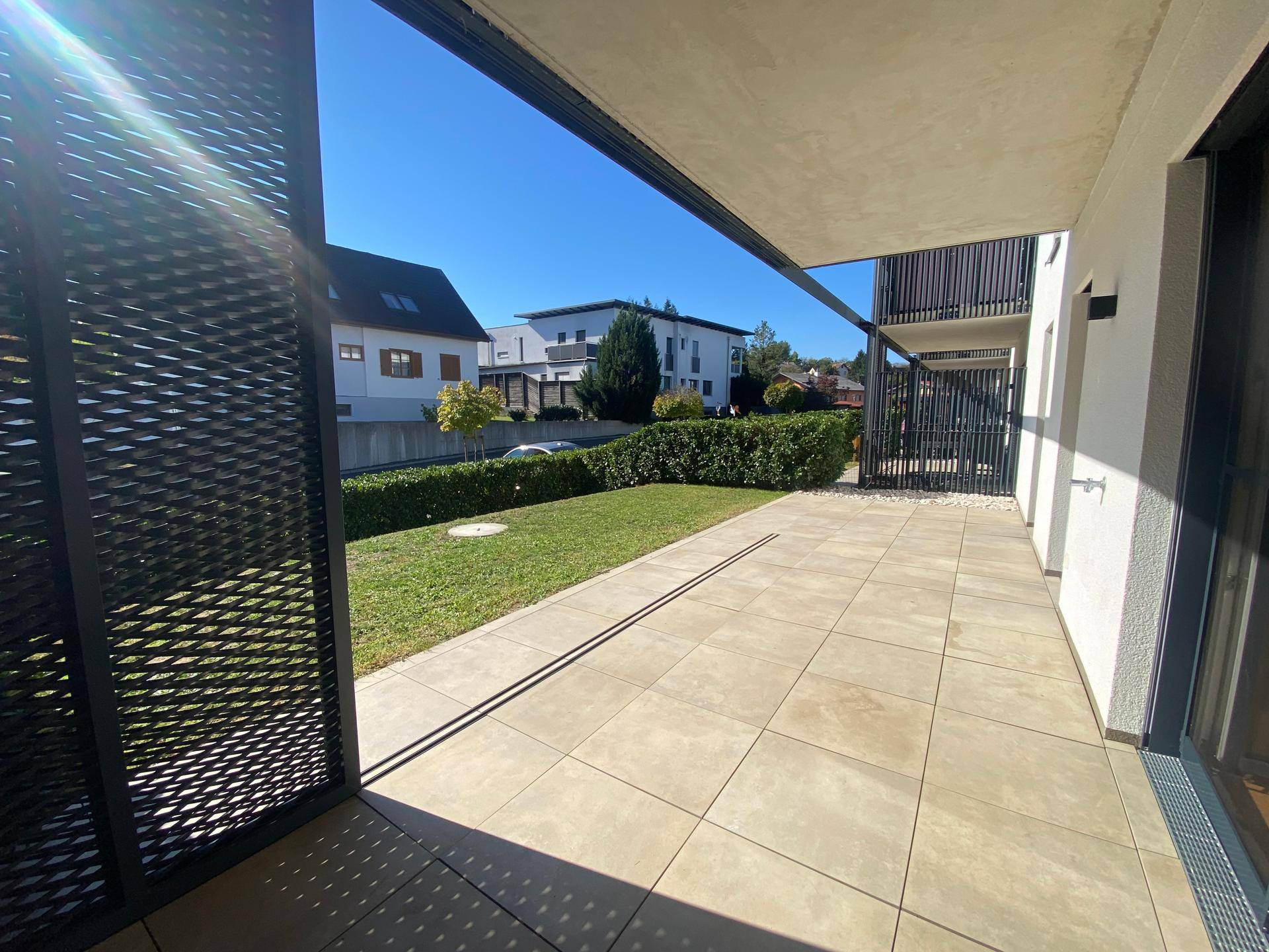 Weitläufige Terrasse mit Fliesenboden und Blick auf die gepflegte Grünfläche und Nachbargebäude.