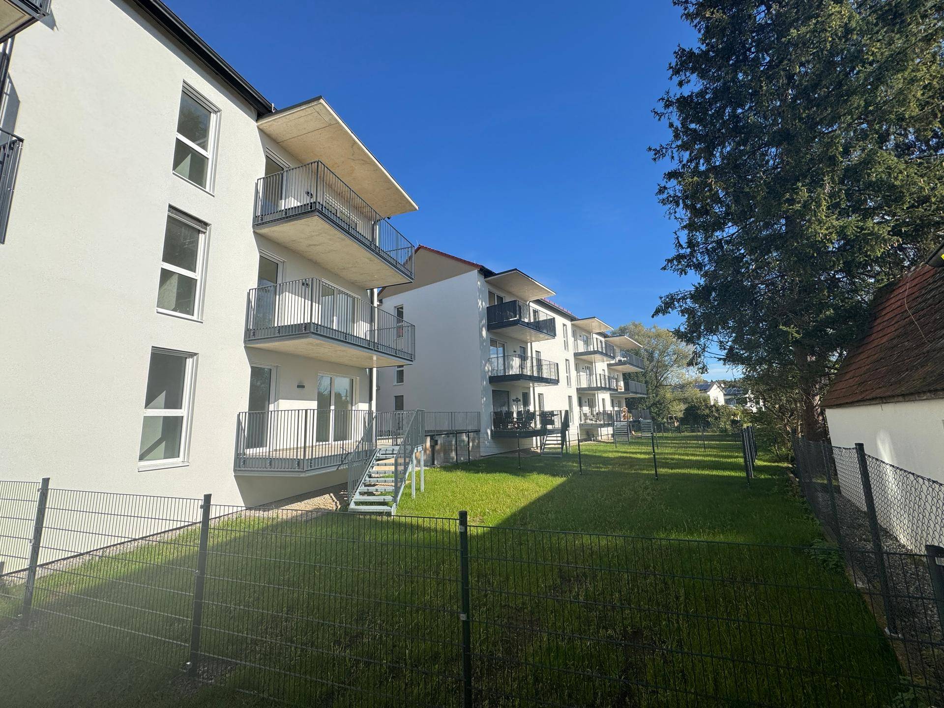 Neue Wohngebäude mit Balkonen und weitläufiger Rasenfläche unter blauem Himmel.