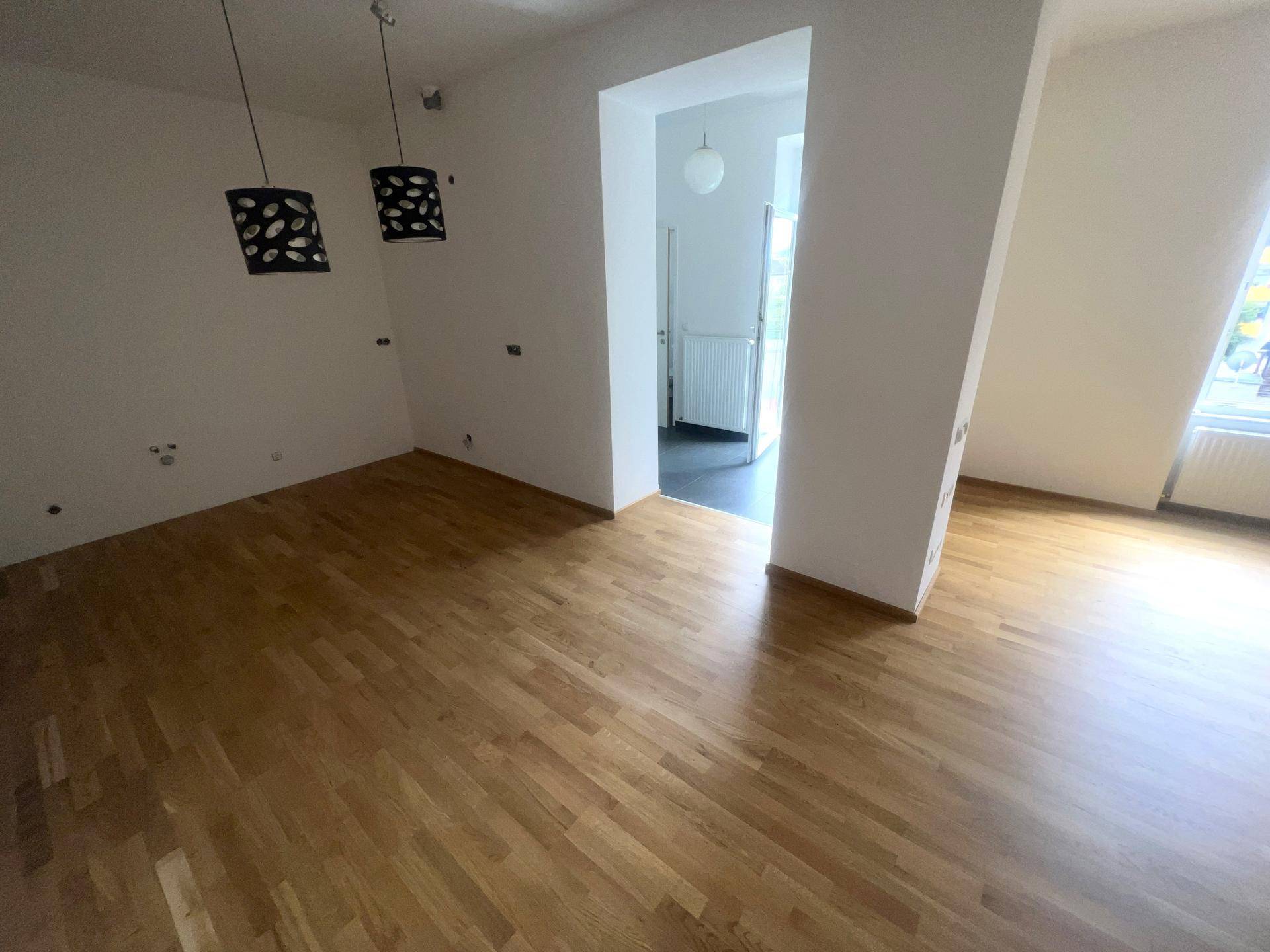 Geräumiges Wohnzimmer mit Parkettboden, modernen Leuchten und offenem Übergang zu anderen Bereichen.
