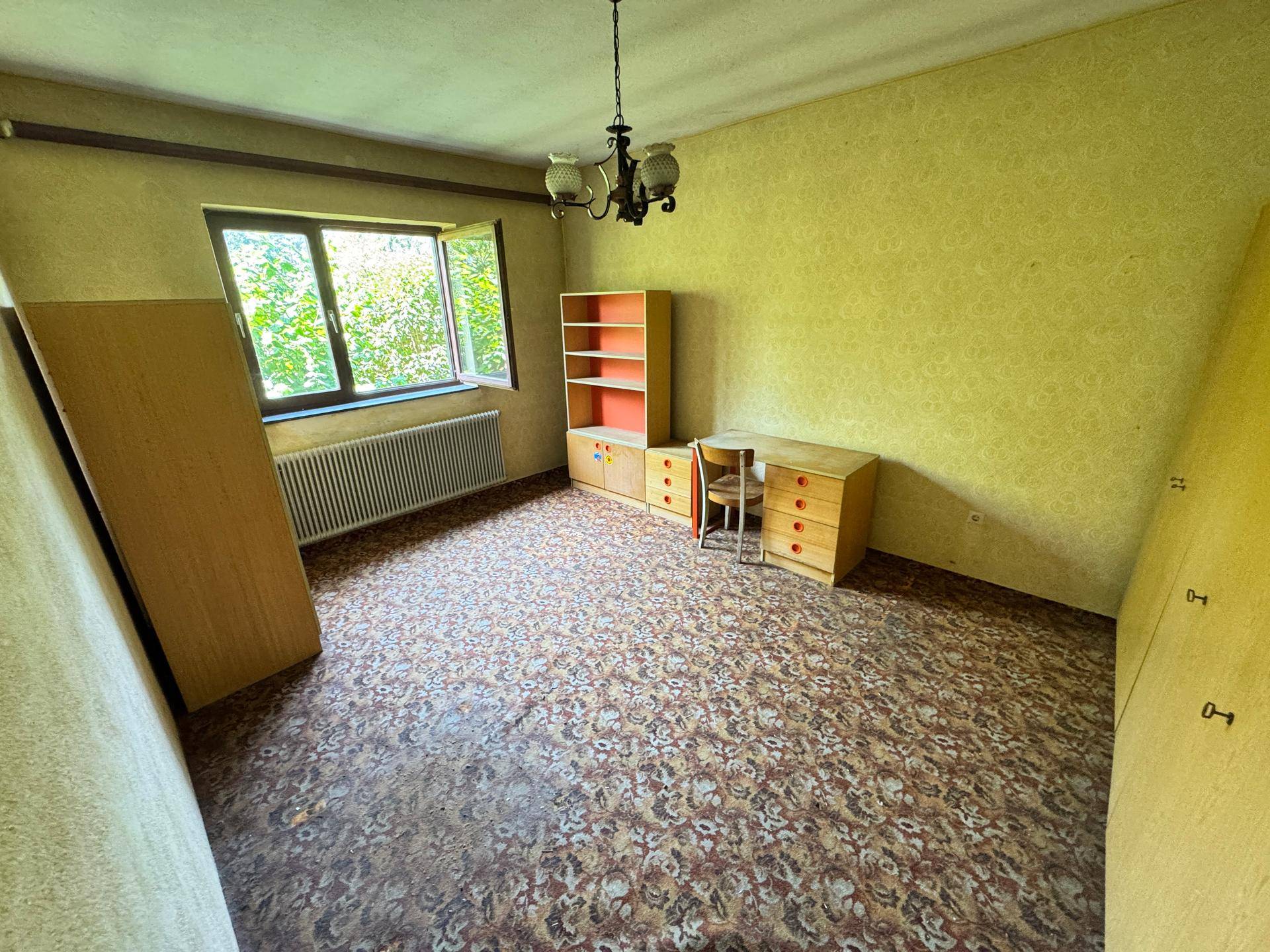 Schlafzimmer mit gemustertem Boden, Schreibtisch und Blick ins Grüne.