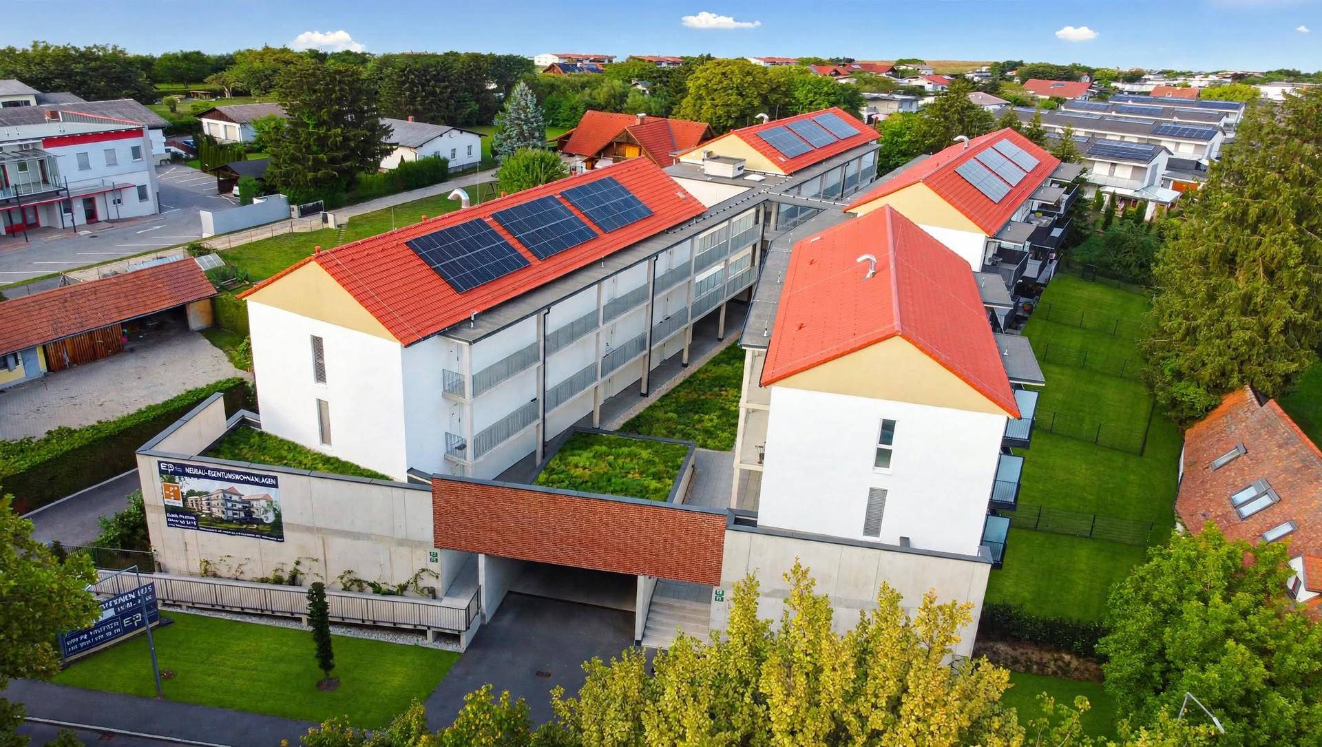 Luftaufnahme eines modernen Wohnkomplexes mit Solaranlagen auf den Dächern und grünen Außenbereichen.