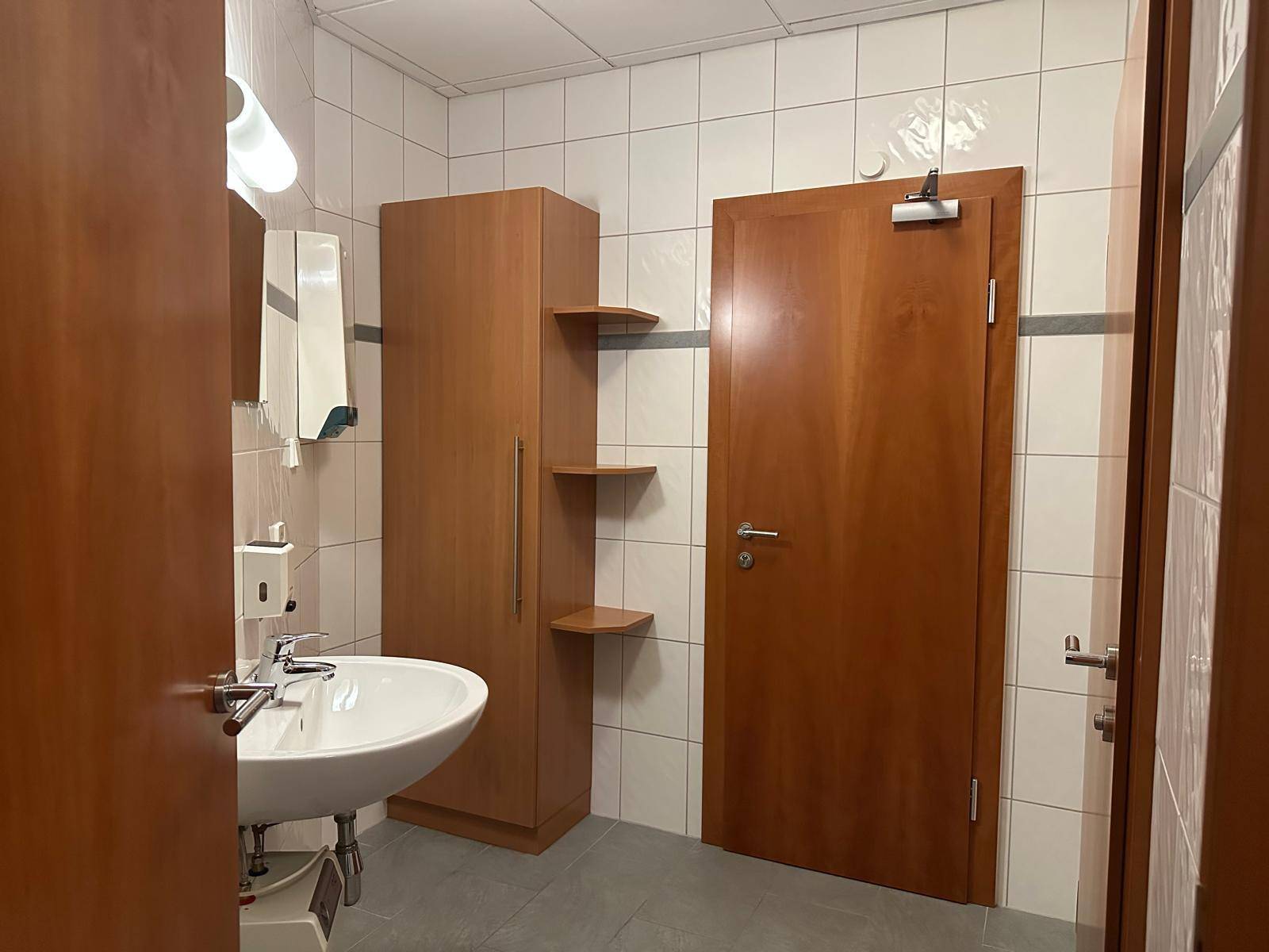 Einfaches WC mit Waschbecken, Fliesenboden und Holzschrank.