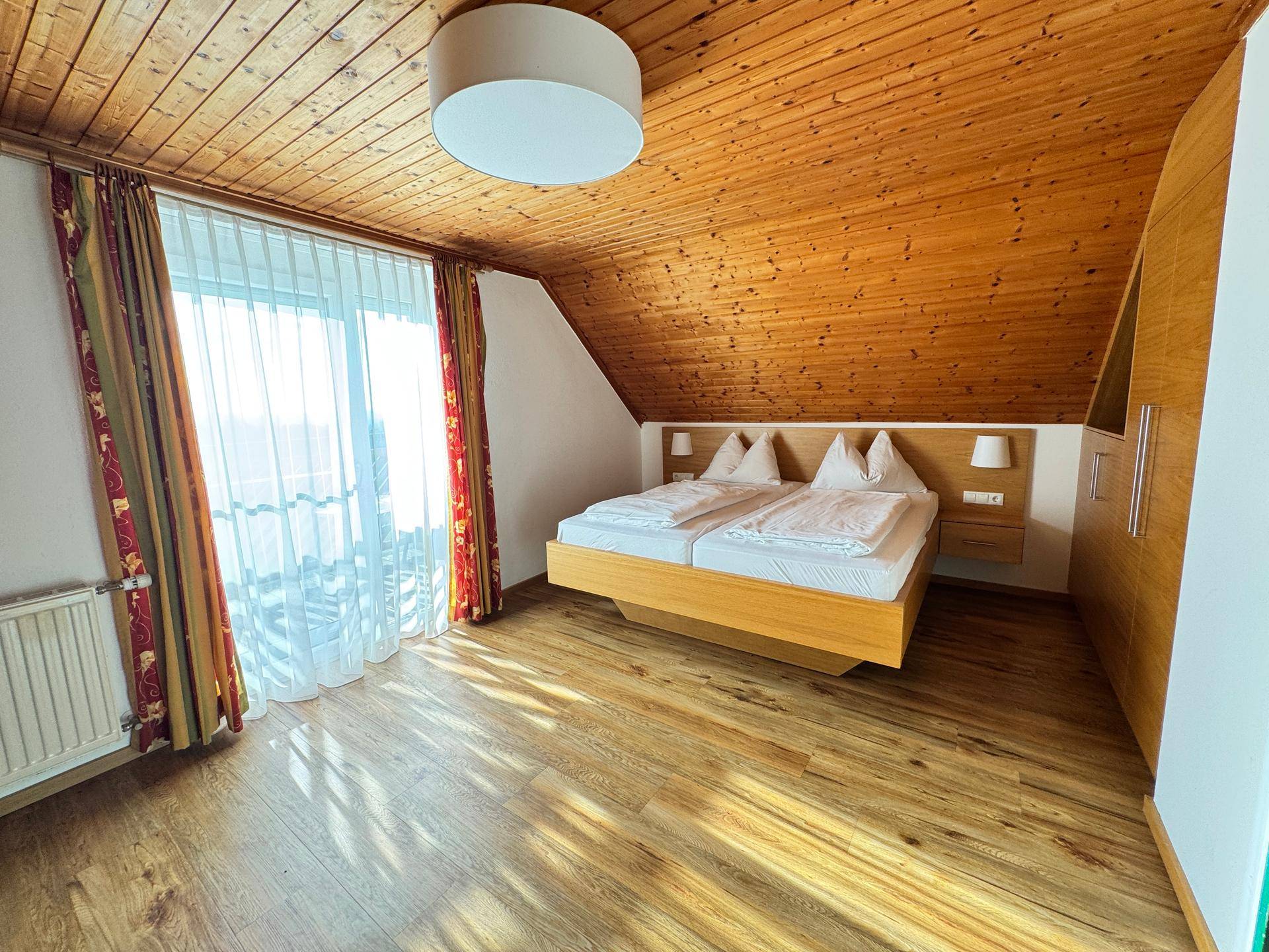 Schlafzimmer mit Holzbalkendecke, Doppelbett und Balkonzugang.