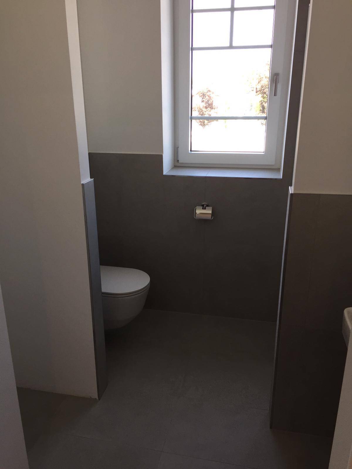 Modernes Gäste-WC mit Wand-WC, grauen Fliesen und Fenster für Tageslicht.