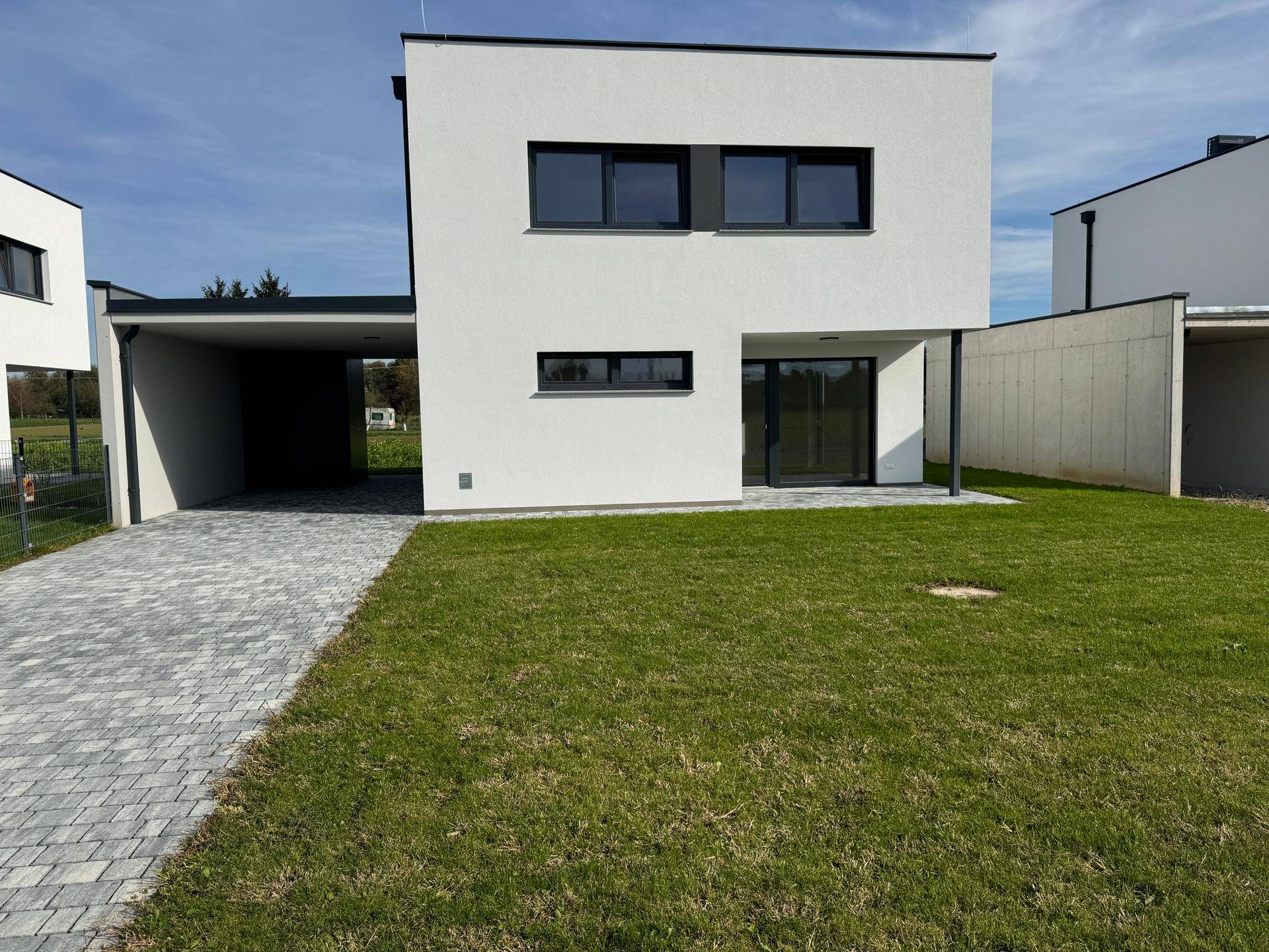 Vorderansicht eines modernen Hauses mit Rasenfläche, gepflasterter Zufahrt und Carport.