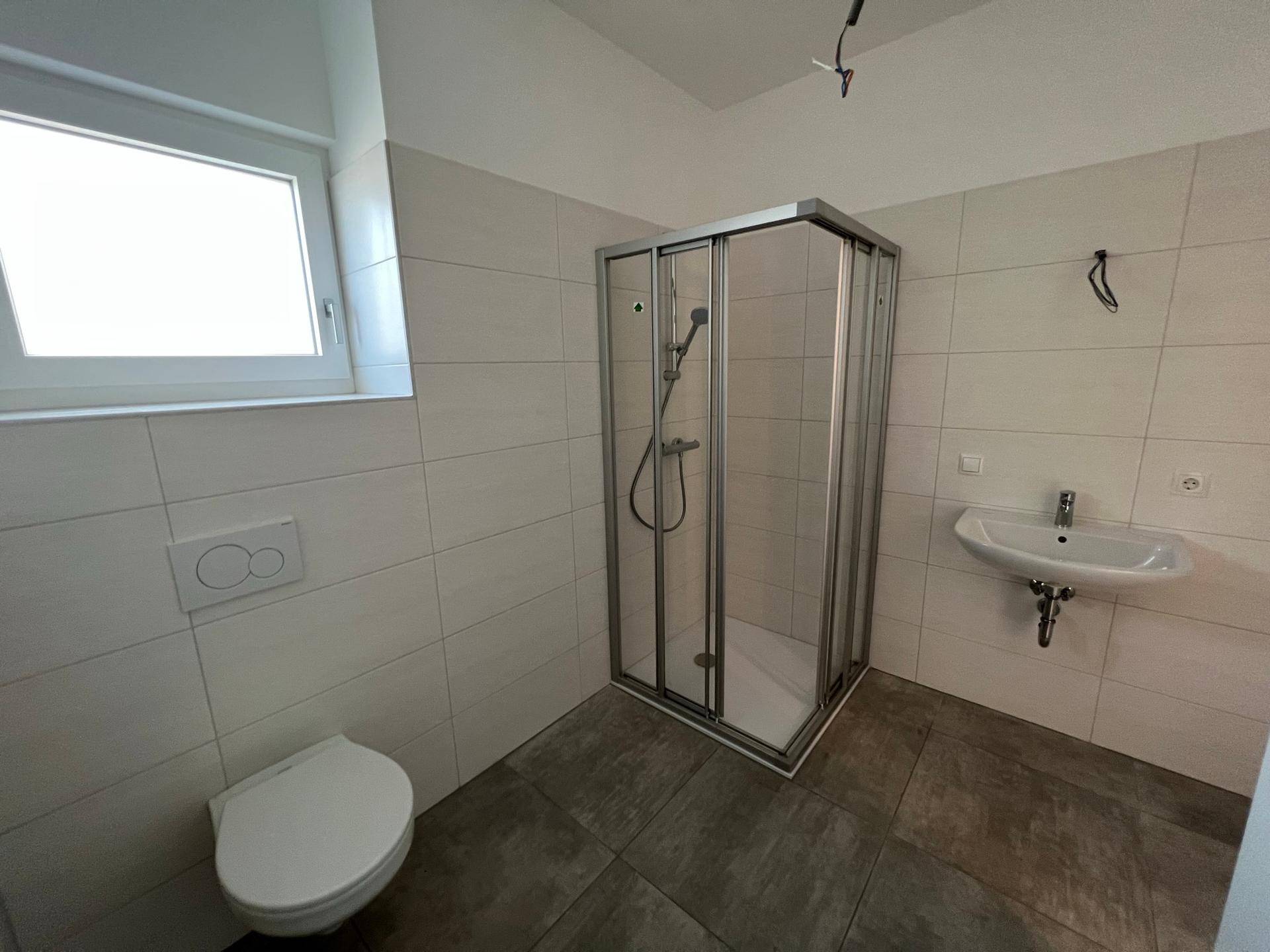 Modernes Badezimmer mit Duschkabine, WC, Waschbecken und Fenster für Tageslicht.