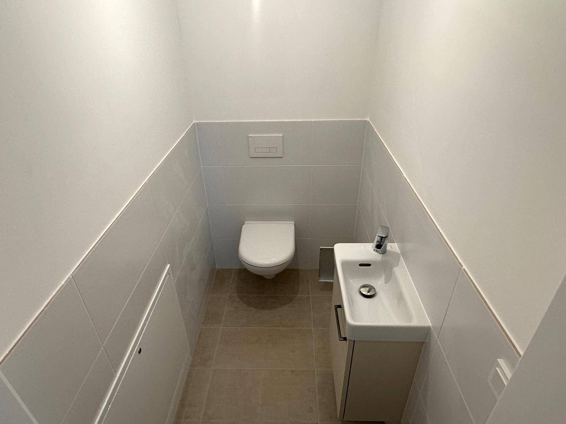 Sauberes Gäste-WC mit wandhängender Toilette und kleinem Handwaschbecken.