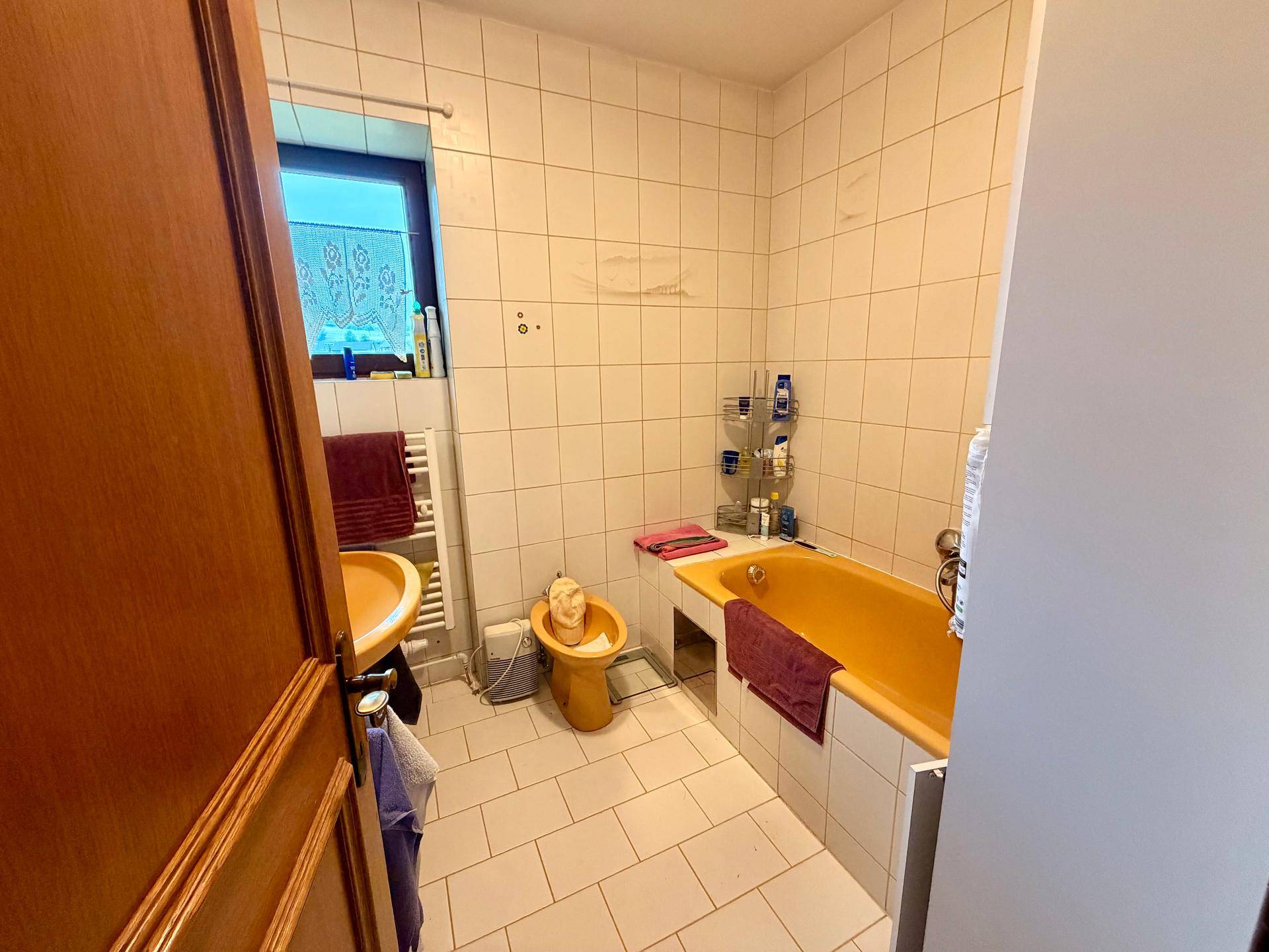 Badezimmer mit gelber Badewanne, Waschbecken und weißen Fliesen, ausgestattet mit einem Fenster.