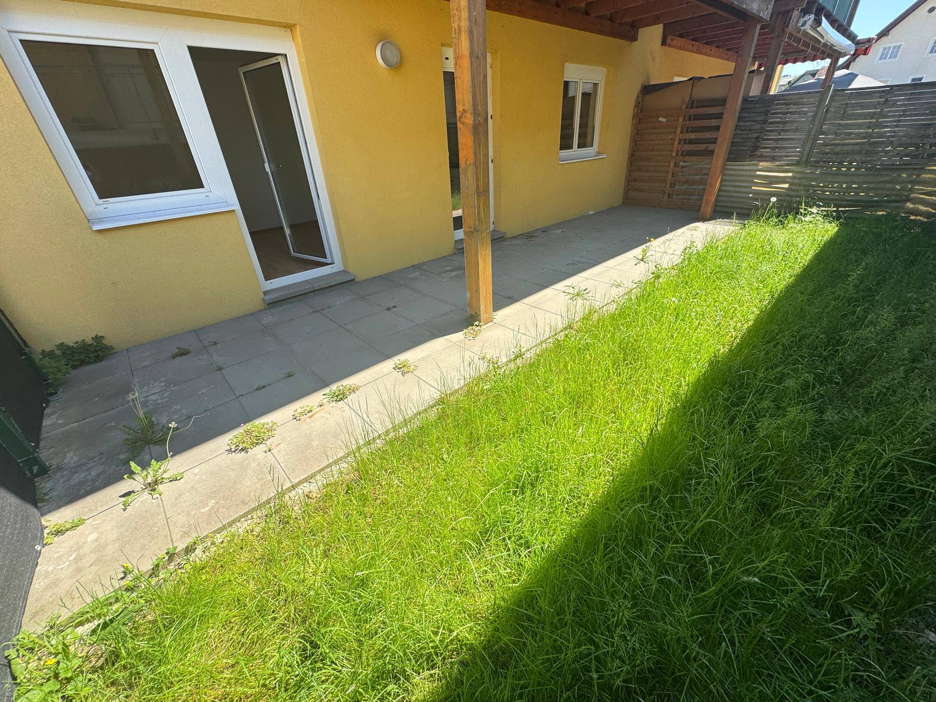 Gepflasterter Weg entlang eines Rasenstreifens mit Zugang zu einer Wohnung im Erdgeschoss.