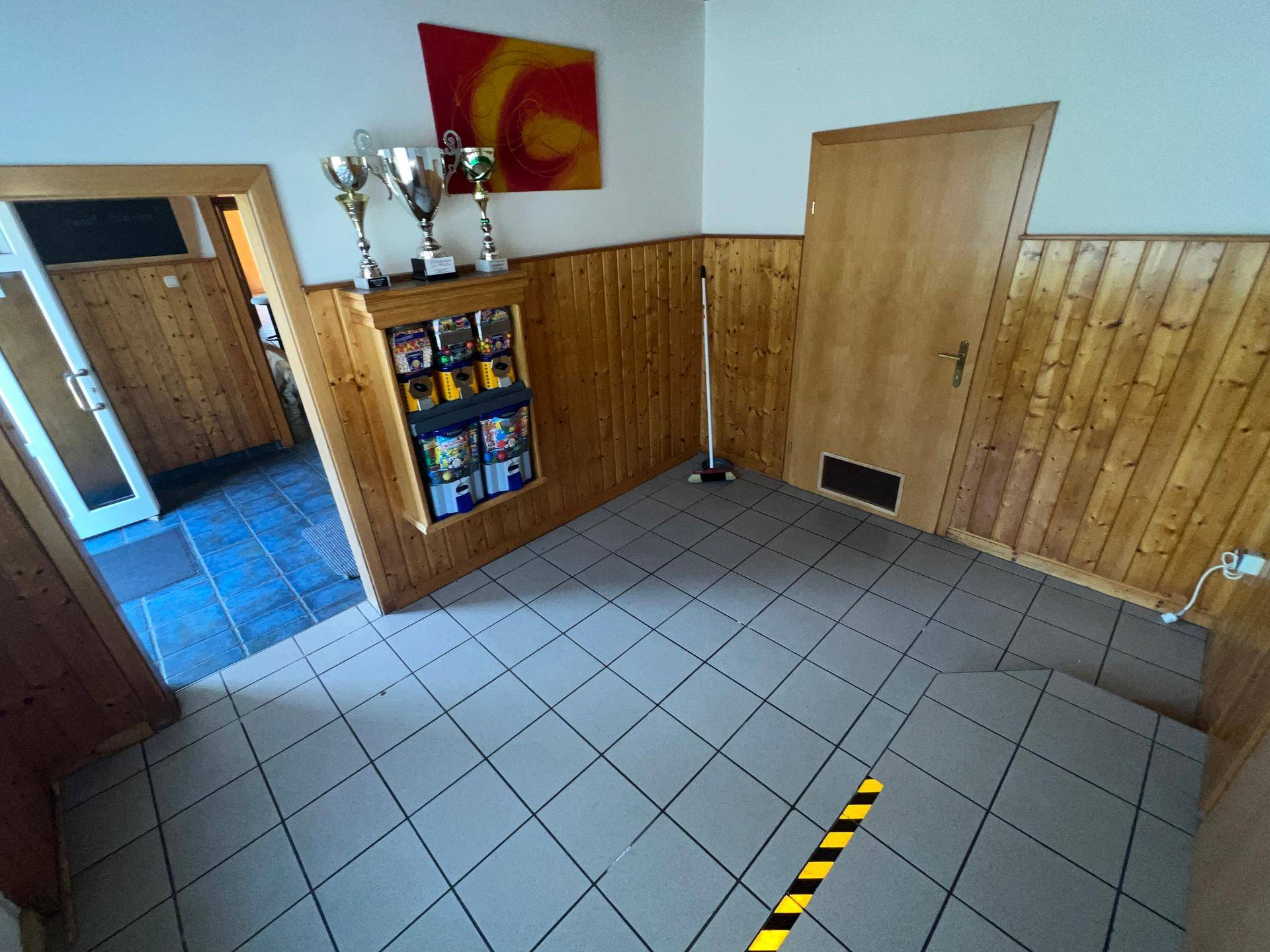Eingangsbereich mit gefliestem Boden, Holztäfelung und Trophäen auf einem Regal.