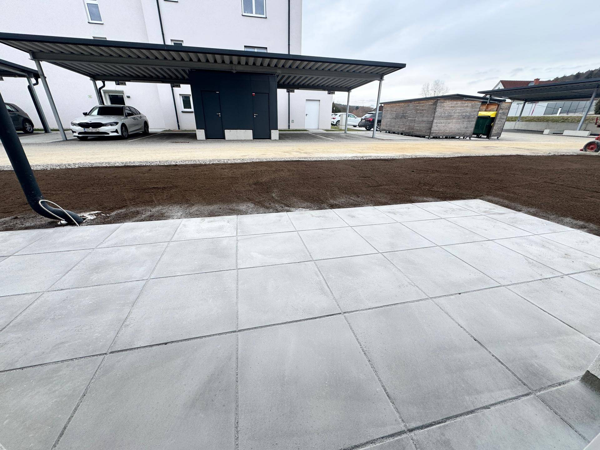 Gepflasterte Terrasse im Erdgeschoss mit Blick auf den Carport und die Außenanlagen.