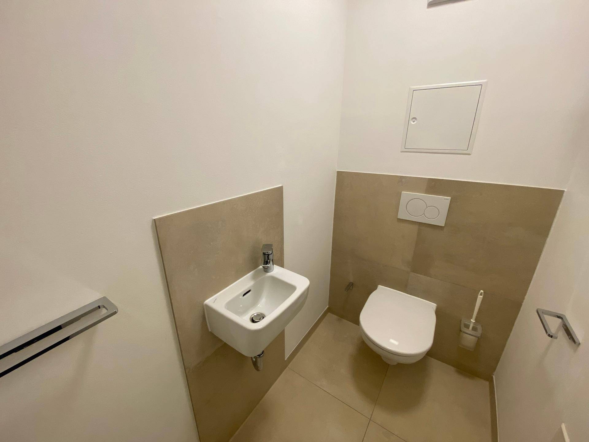Separates Gäste-WC mit Wand-WC, kleinem Waschbecken und beigefarbenen Akzentfliesen.