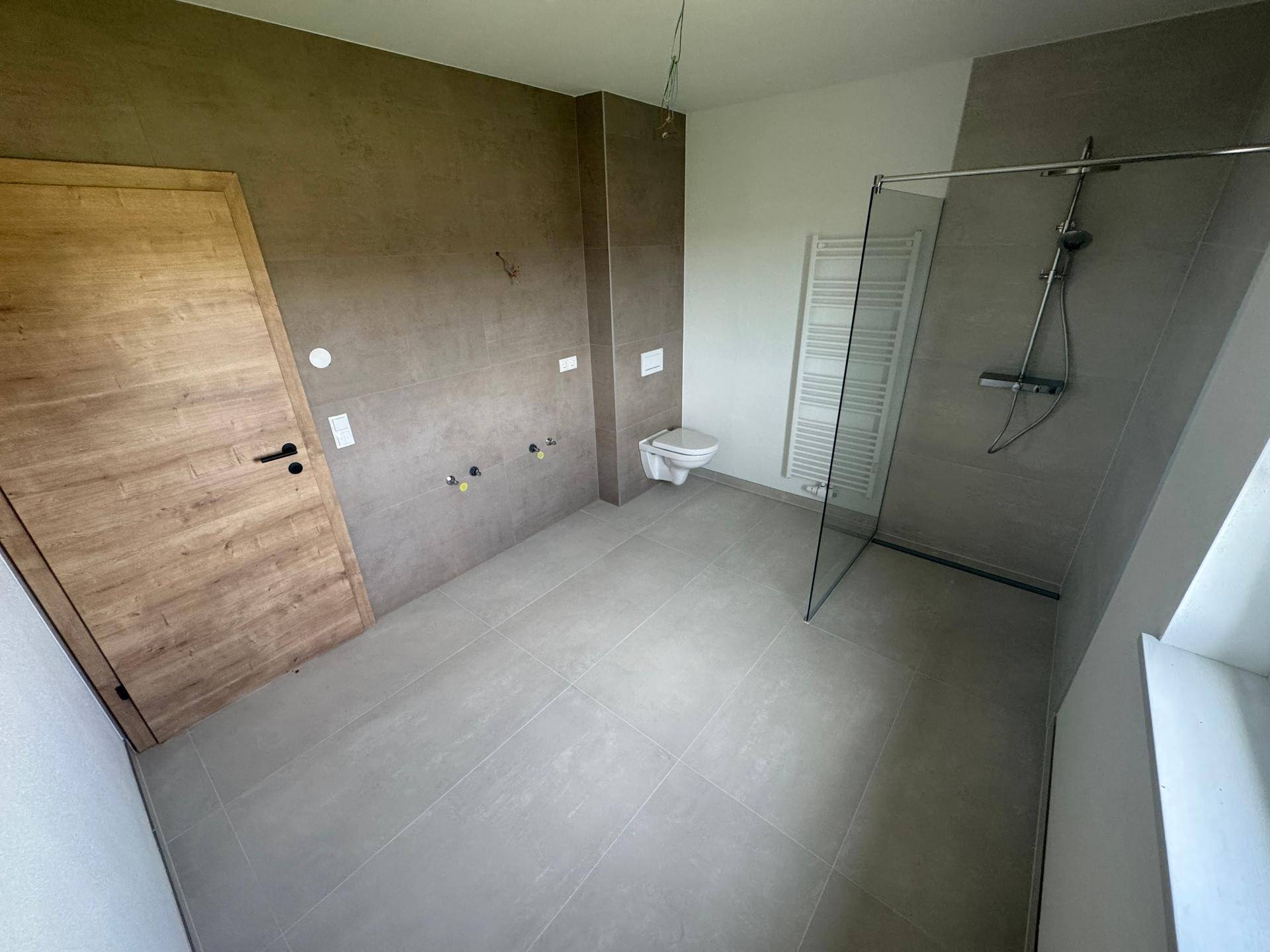 Modernes Badezimmer mit grauen Fliesen, Wand-WC und ebenerdiger Dusche.