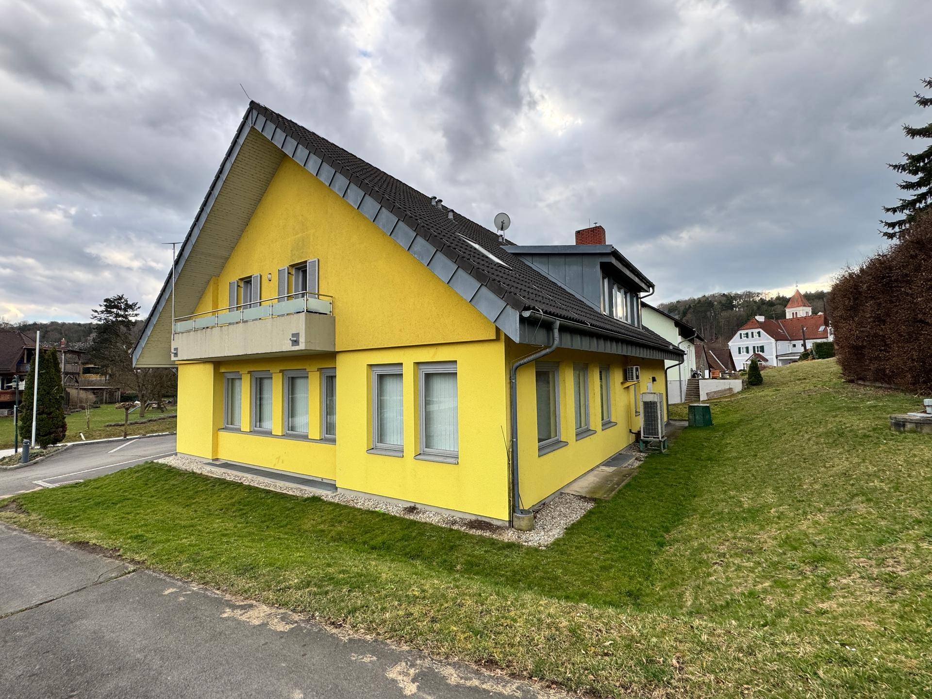 Seitenansicht des gelben Gebäudes mit grünem Rasen und einem kleinen Balkon.