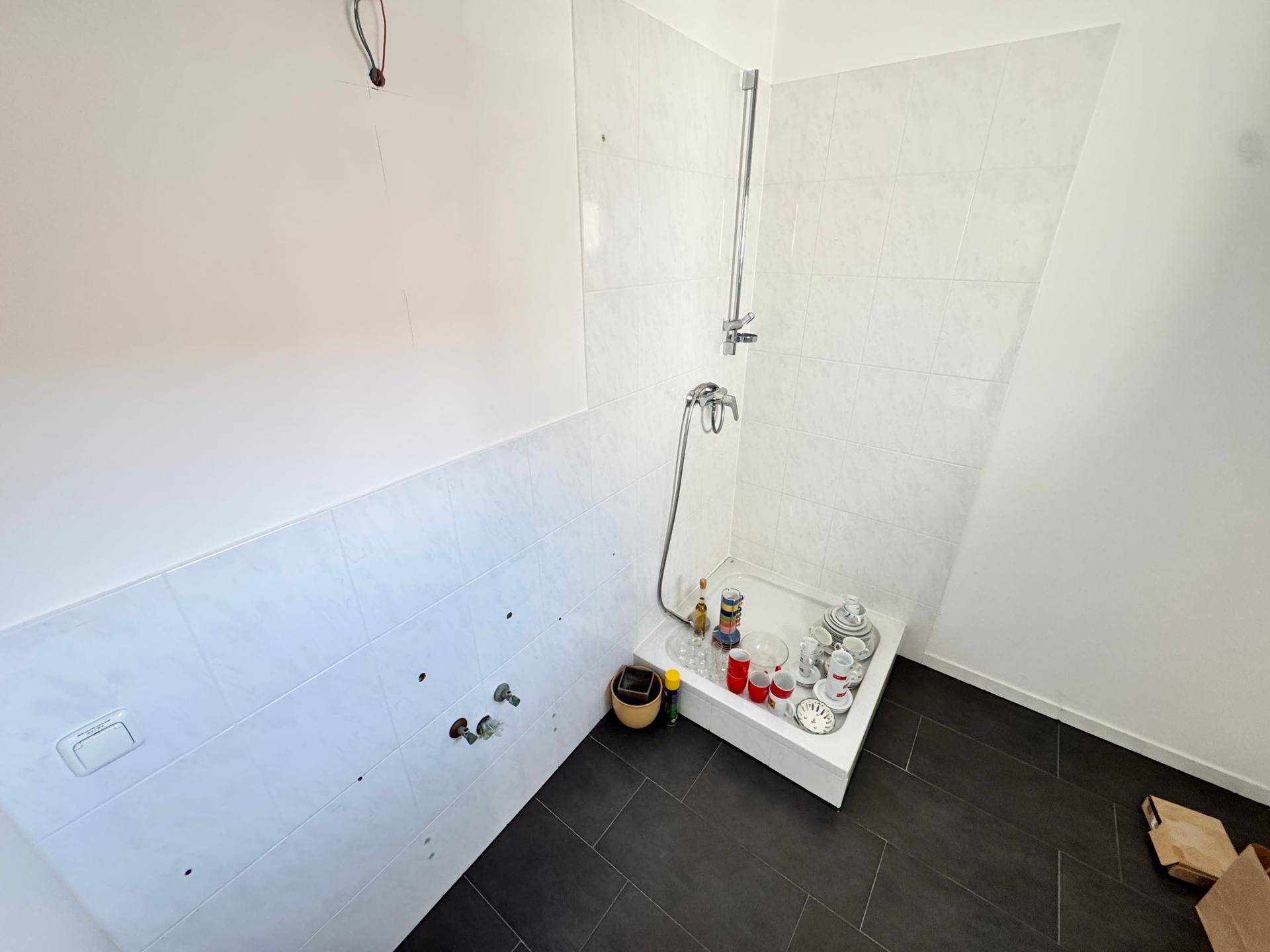 Helles Badezimmer mit Duschbereich und dunklen Bodenfliesen, noch im Ausbau oder unvollendet, aber modern.