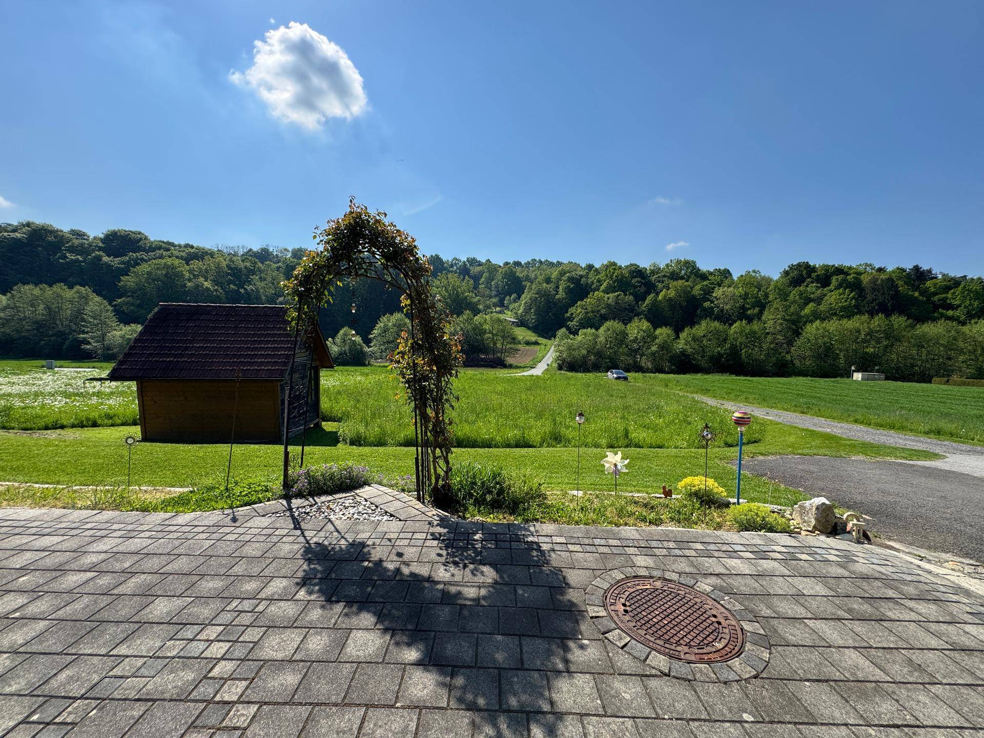 Gepflasterte Terrasse mit Rosenbogen und weitem Blick über grüne Felder und Landschaft.
