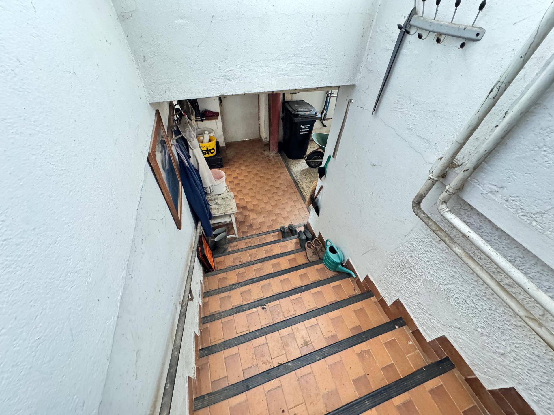 Treppenabgang in den Keller mit gefliesten Stufen und weiß gestrichenen Wänden.