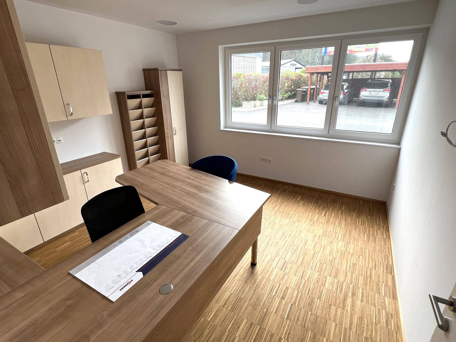 Helles Büro mit Holzboden, modernen Möbeln und großen Fenstern mit Blick ins Grüne.
