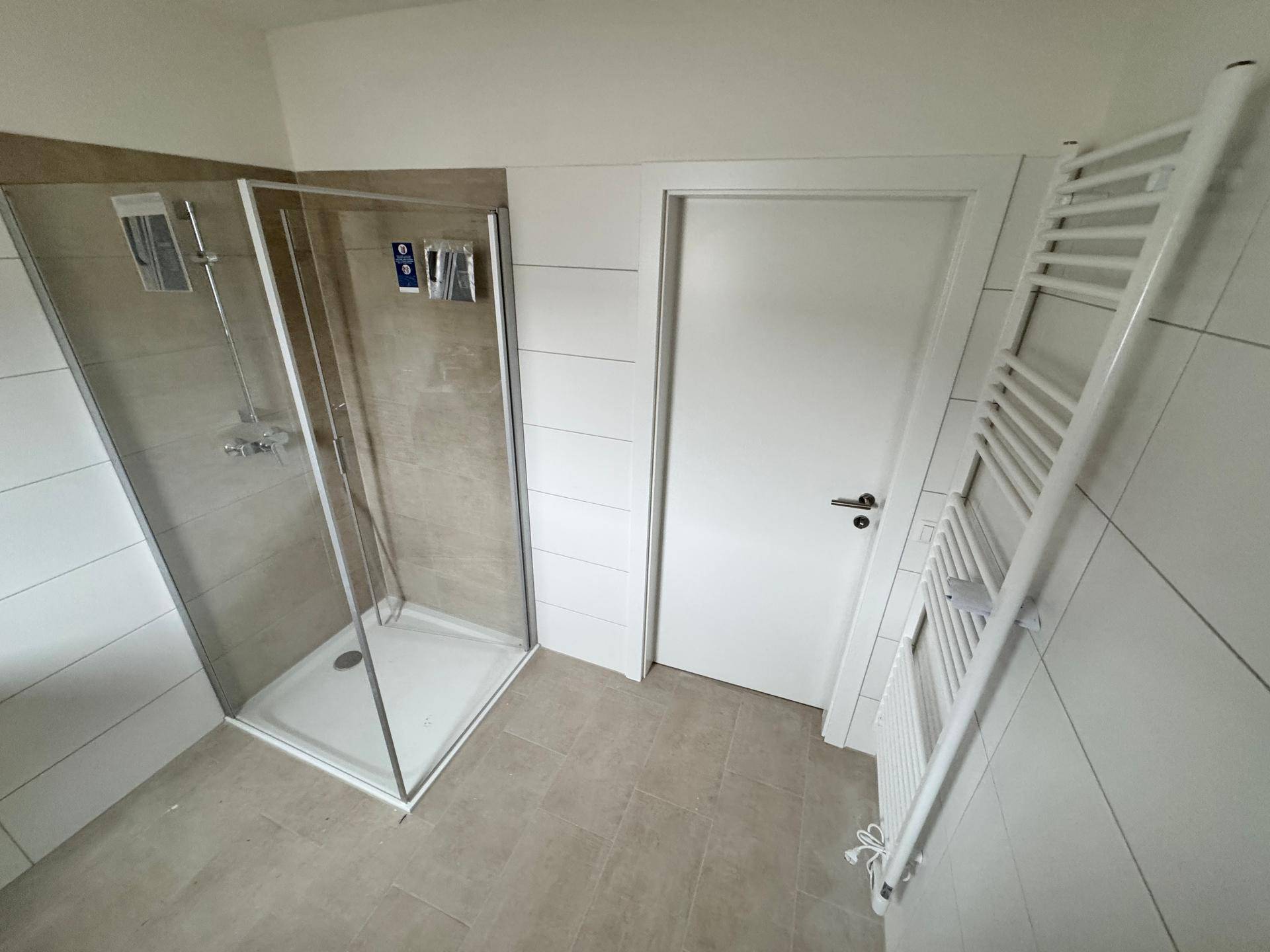 Modernes Badezimmer mit Duschkabine, weißen Fliesen und beheiztem Handtuchhalter.