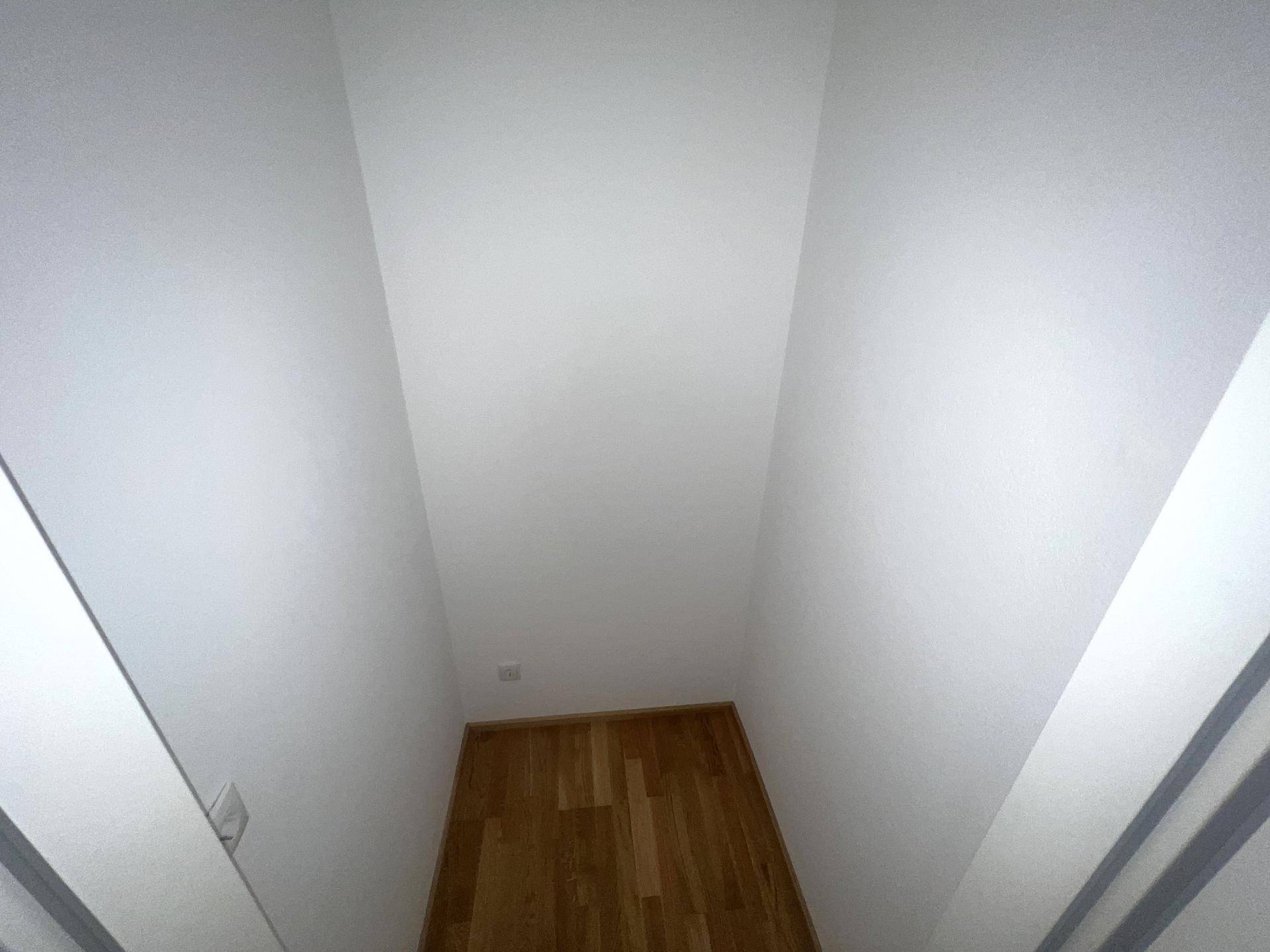 Schmaler Flur mit Parkettboden und weißen Wänden, der zu einem weiteren Bereich führt.