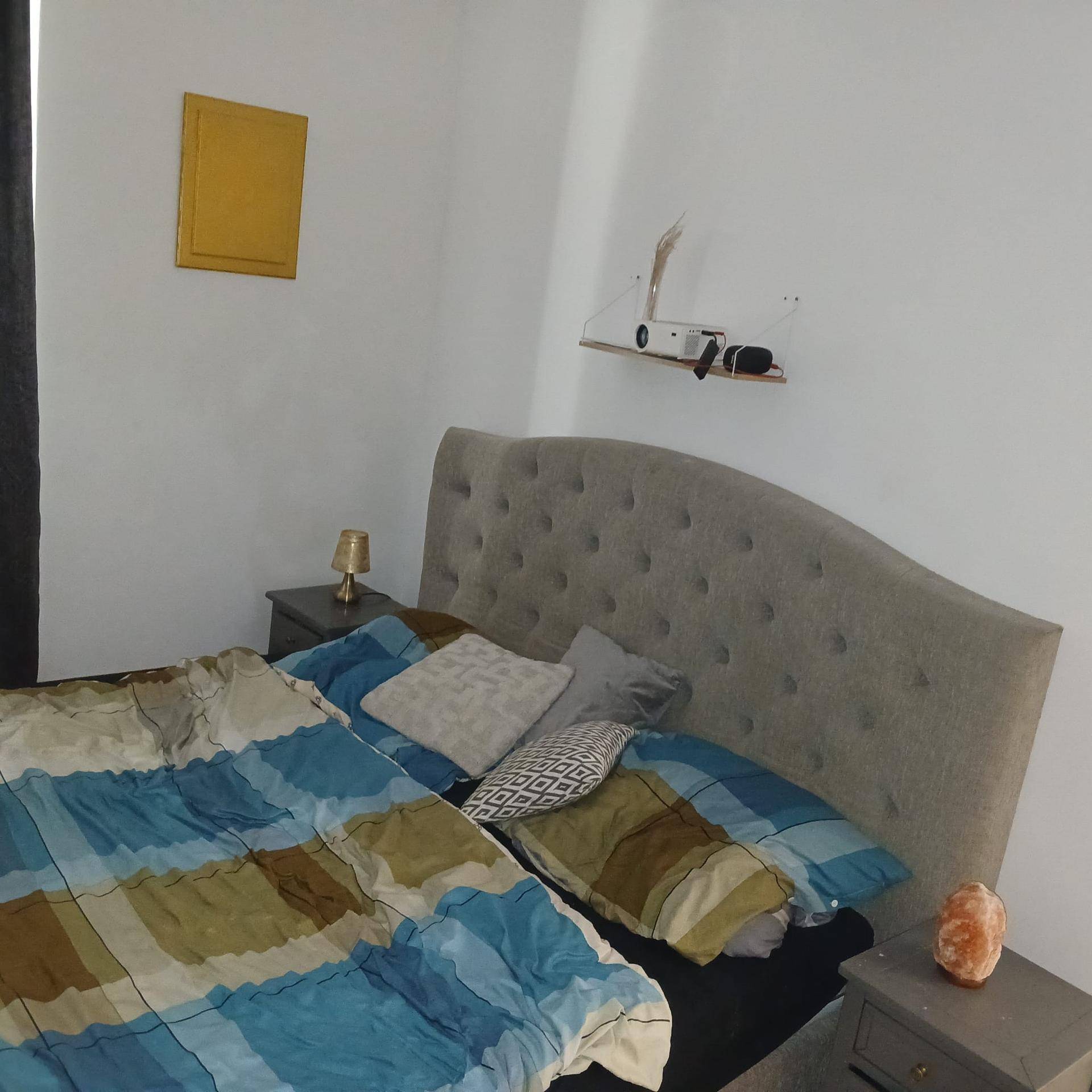 Schlafzimmer mit großem, gepolstertem Bett, Nachttischen und schlichter Wandgestaltung.