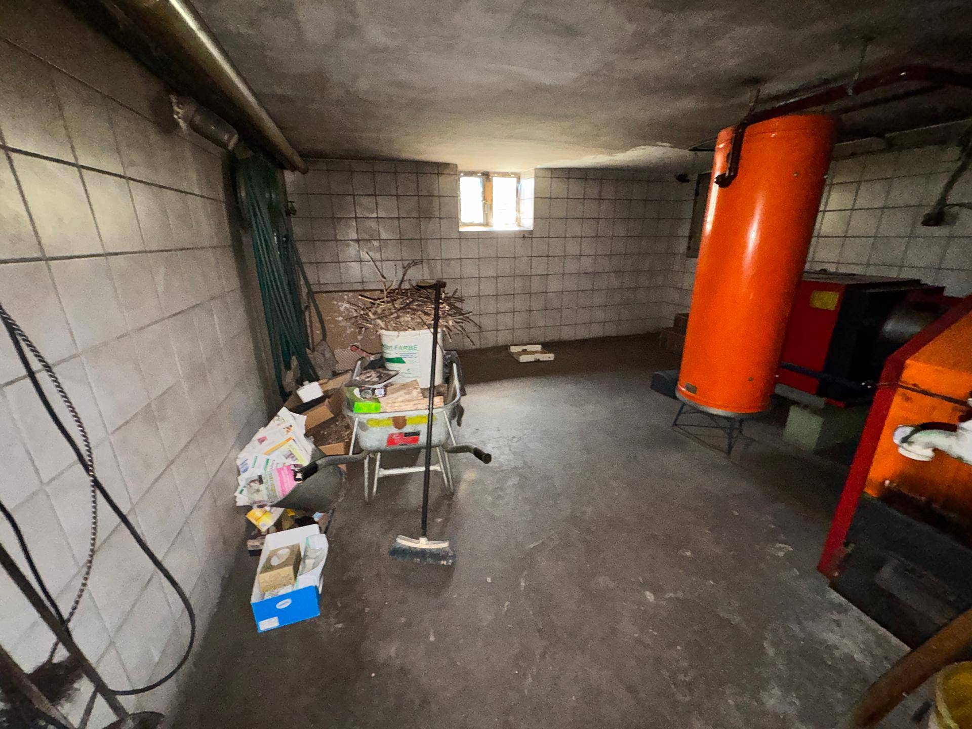Kellerraum mit gefliesten Wänden, Betonboden und einem orangefarbenen Warmwasserspeicher.
