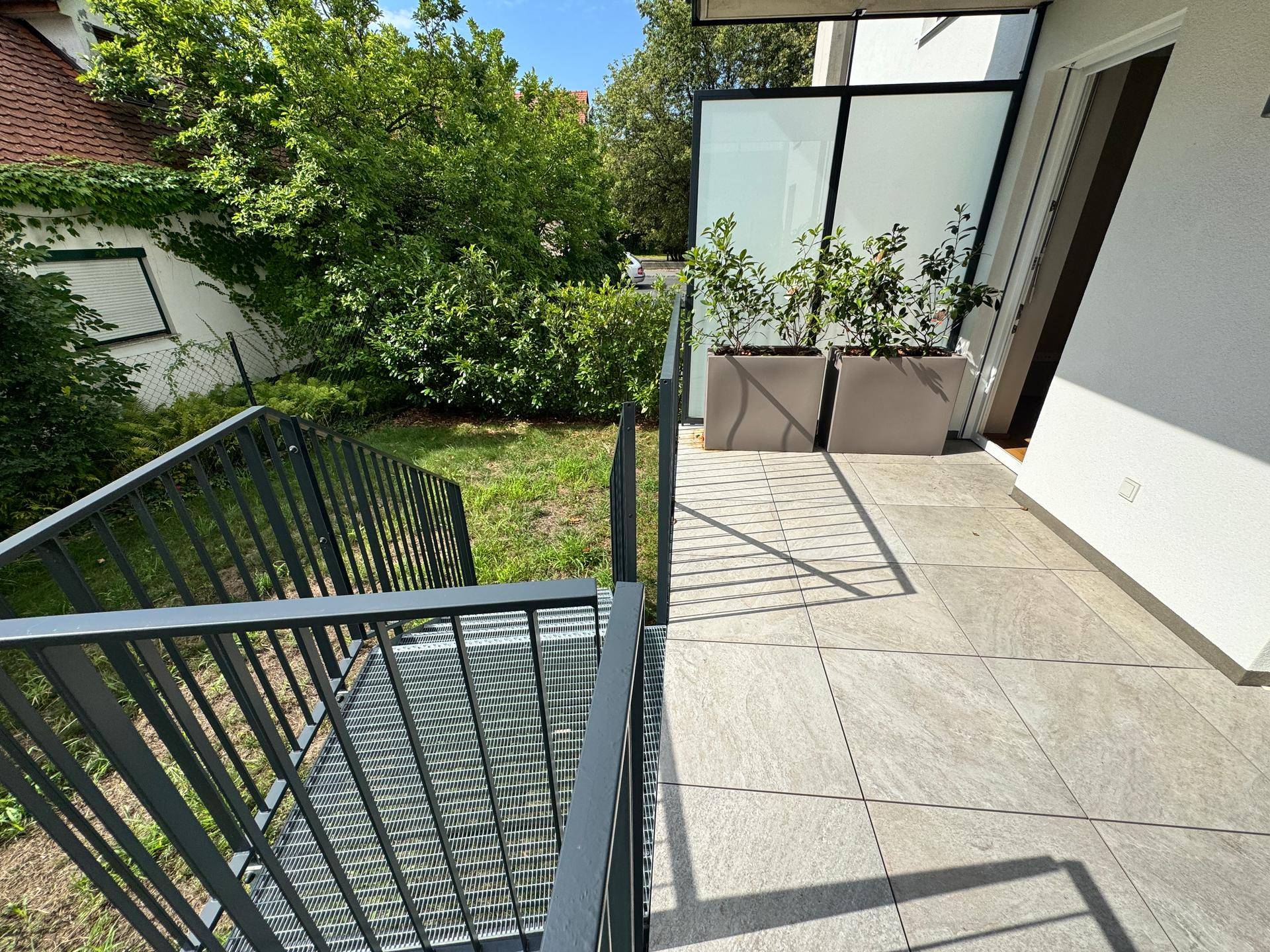 Geräumige Terrasse mit Fliesenboden und Treppe, die zum privaten Gartenbereich führt.