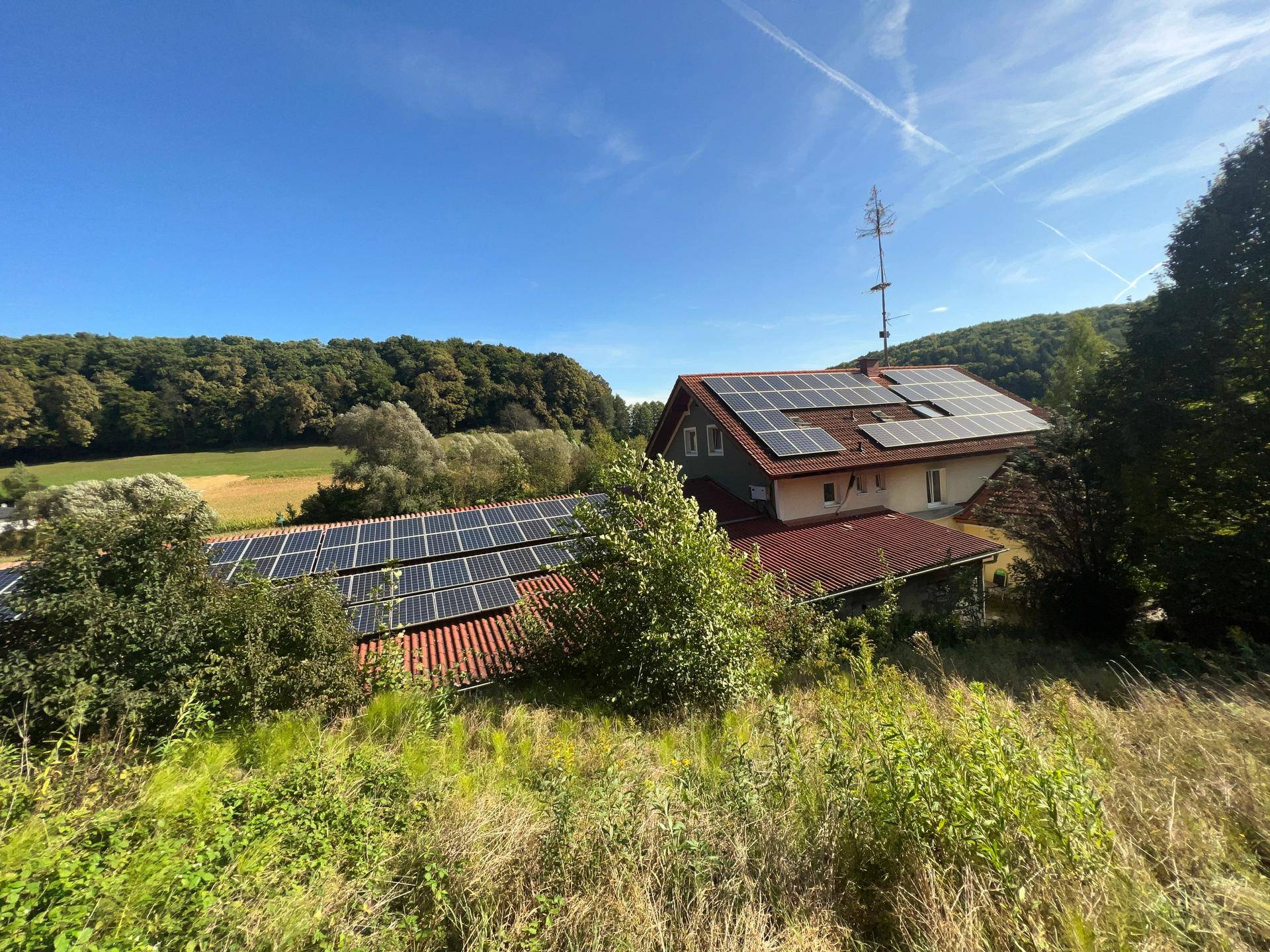 Dachansicht des Gebäudes mit zahlreichen Photovoltaik-Modulen und umgebender grüner Landschaft.