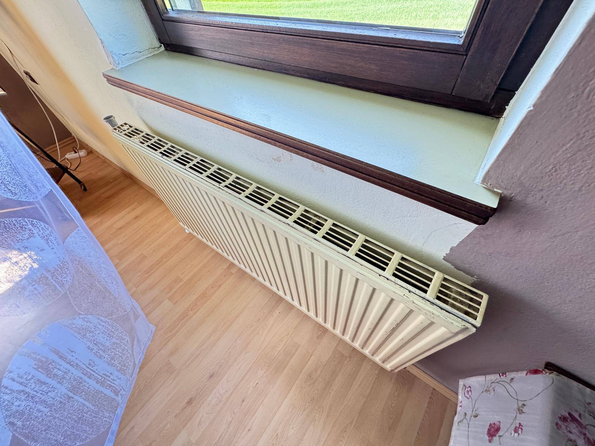 Heizkörper unter einem Fenster mit Holzboden, der für Wärme im Raum sorgt.