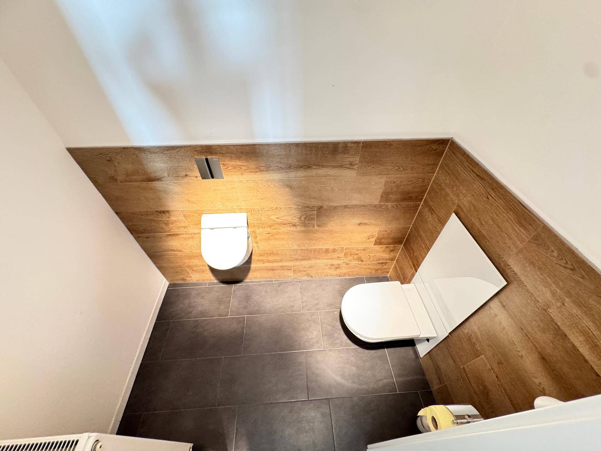 Modernes WC mit dunklen Fliesen und Holzoptik-Wandverkleidung, minimalistisch und funktional gestaltet.