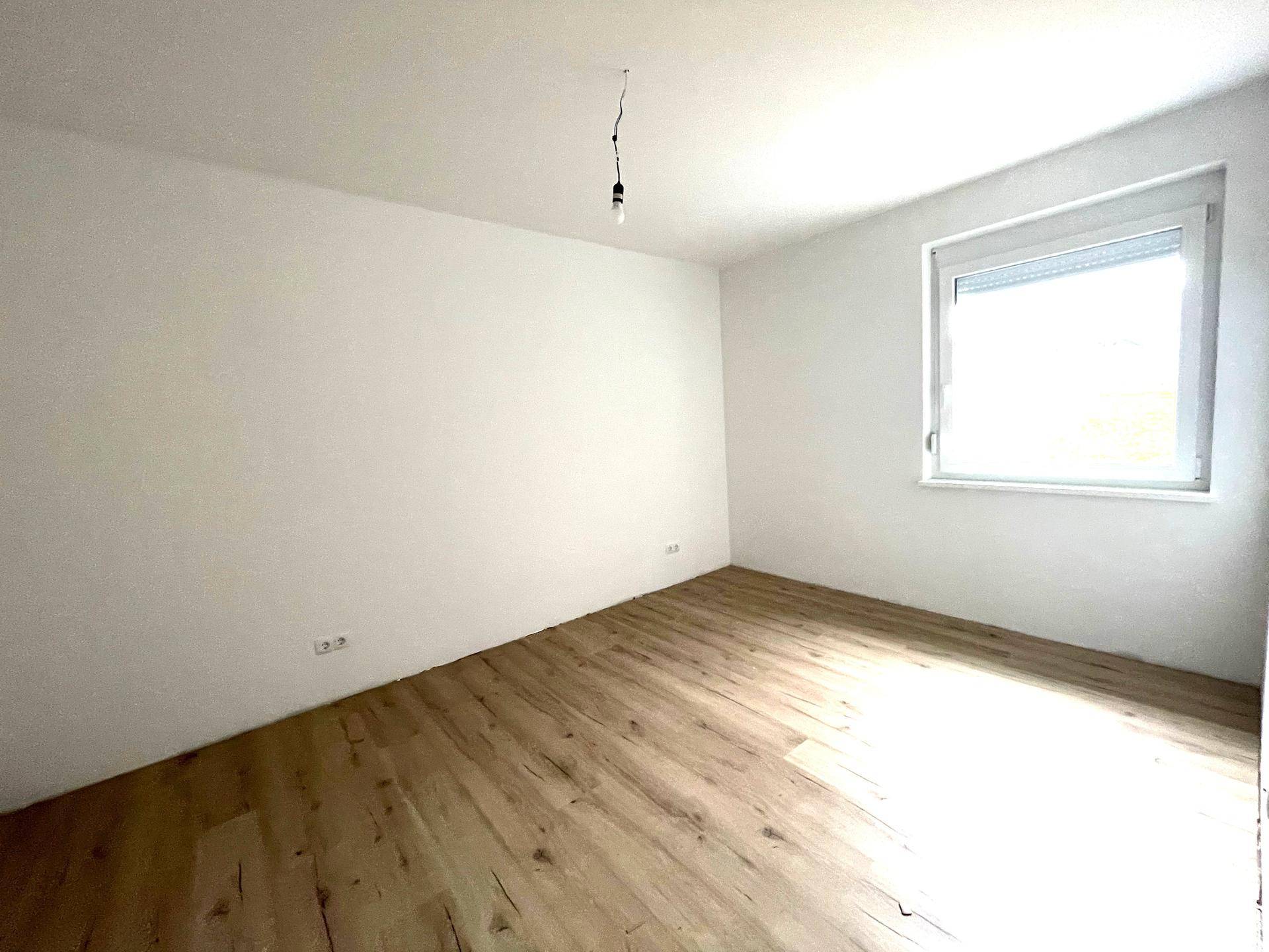 Helles Schlafzimmer mit Laminatboden und Fenster, ausgestattet mit einem Rollladen für Privatsphäre.