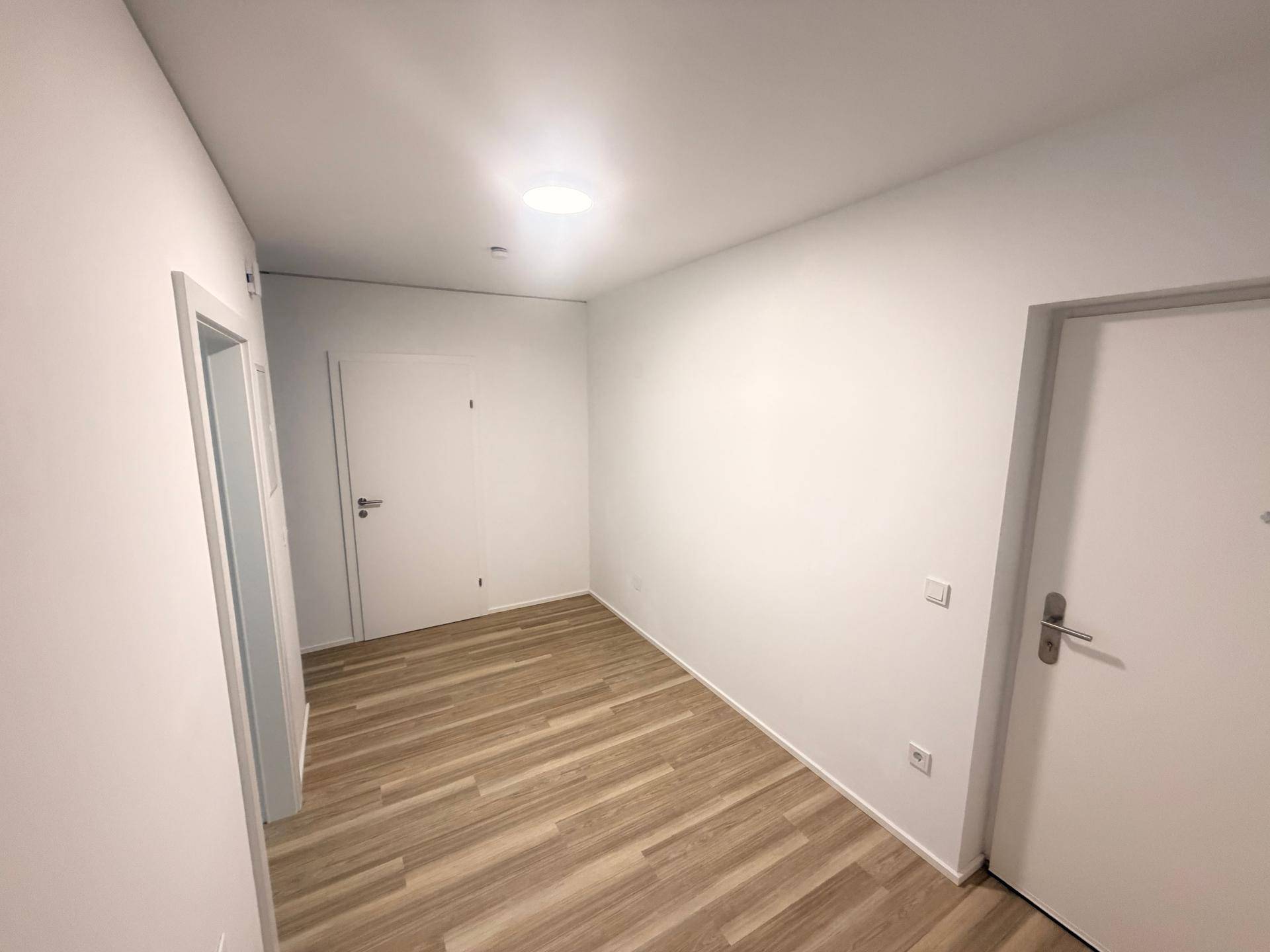 Heller Flur mit modernem Laminatboden und weißen Wänden.