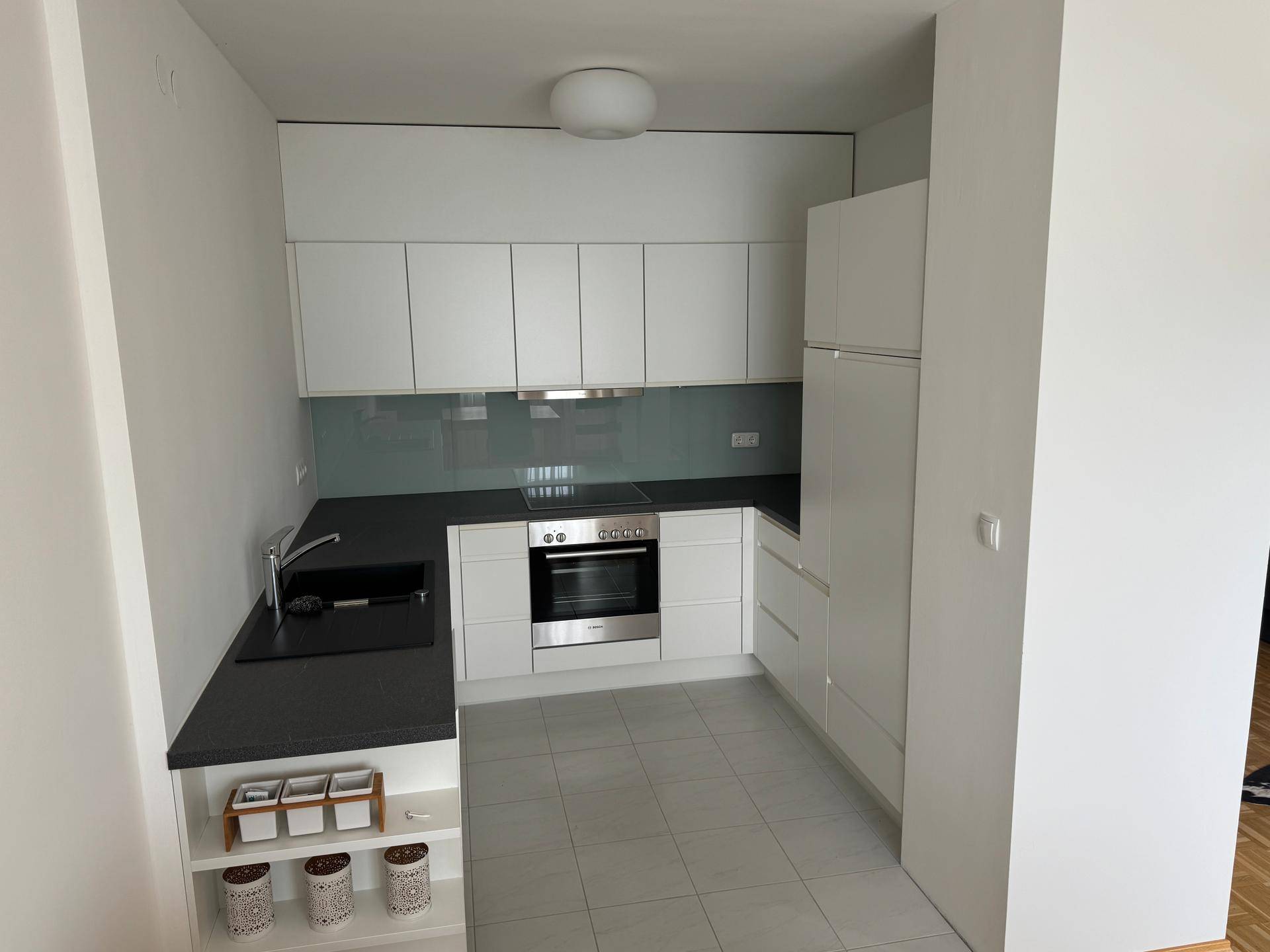 Moderne Einbauküche mit weißen Hochglanzfronten, dunkler Arbeitsplatte und Fliesenboden.