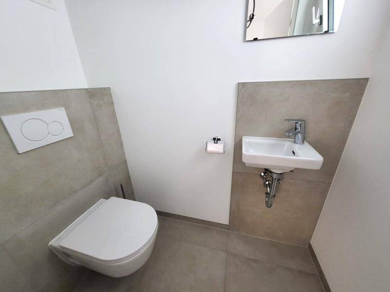 Gäste-WC mit modernem Wand-WC, kleinem Waschbecken und hellen Fliesen.