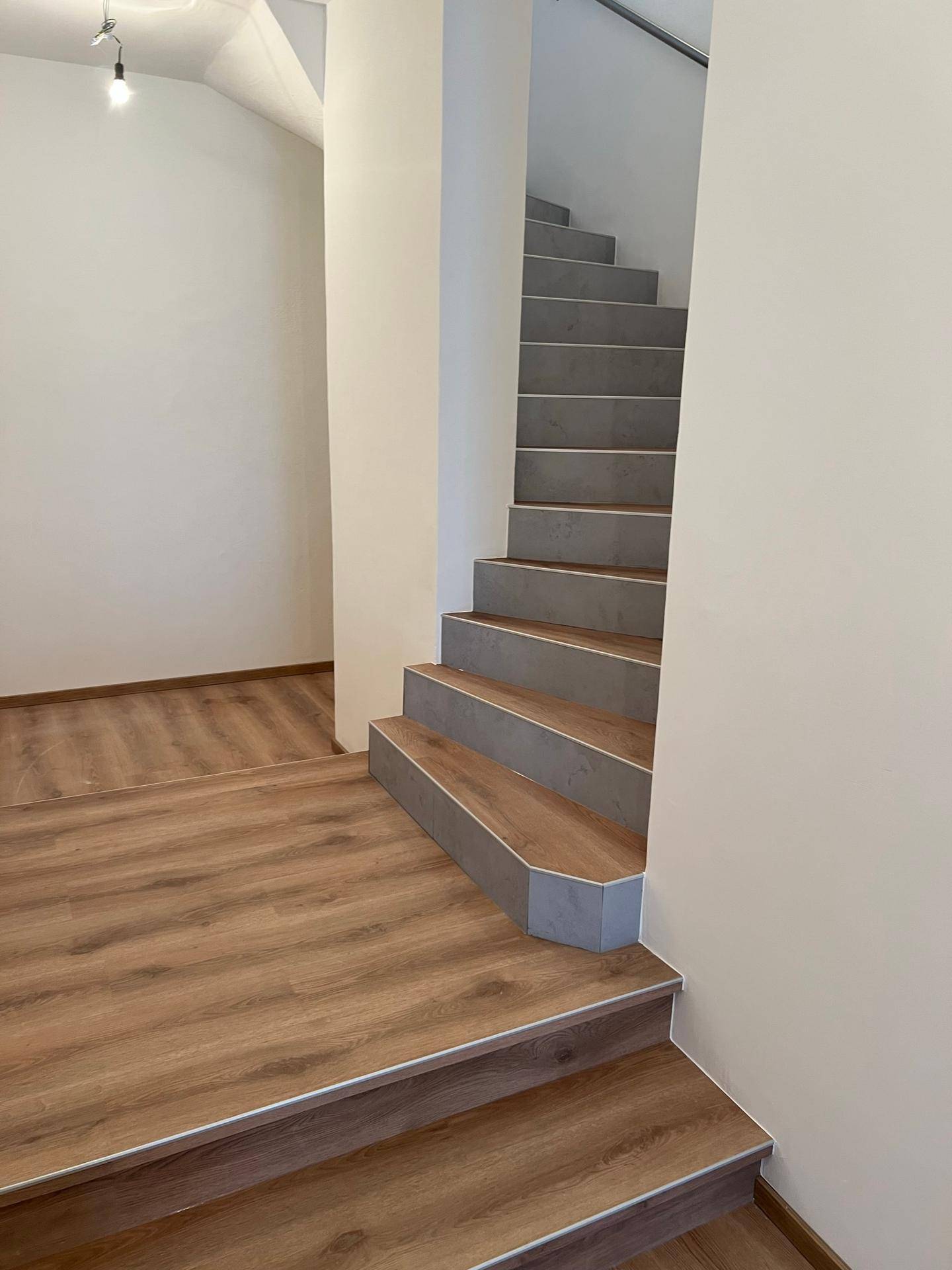 Moderne Treppe mit hellgrauen Stufen und Laminatboden im Flur, die zu den oberen Etagen führt.
