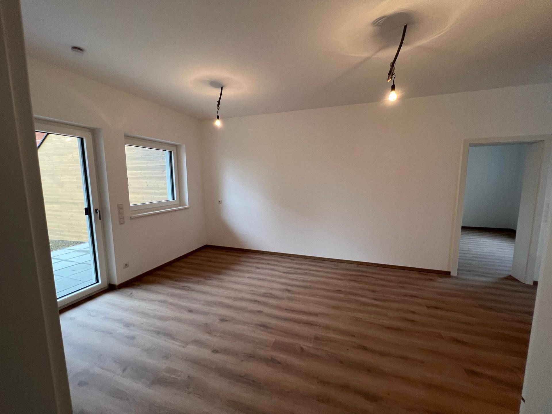 Geräumiges Wohnzimmer mit Laminatboden, großen Fenstern und Zugang zu einem Außenbereich.