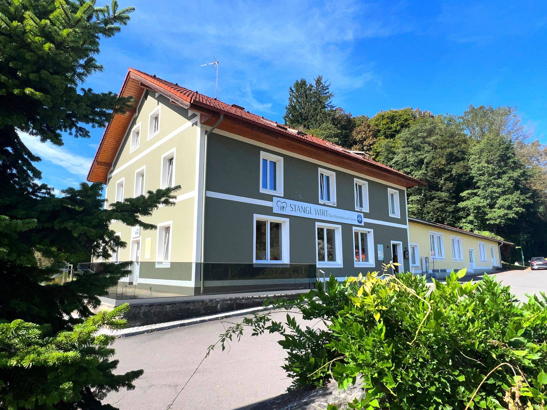Das Gebäude präsentiert sich mit einer frisch gestrichenen Fassade in Grün und Beige unter blauem Himmel.